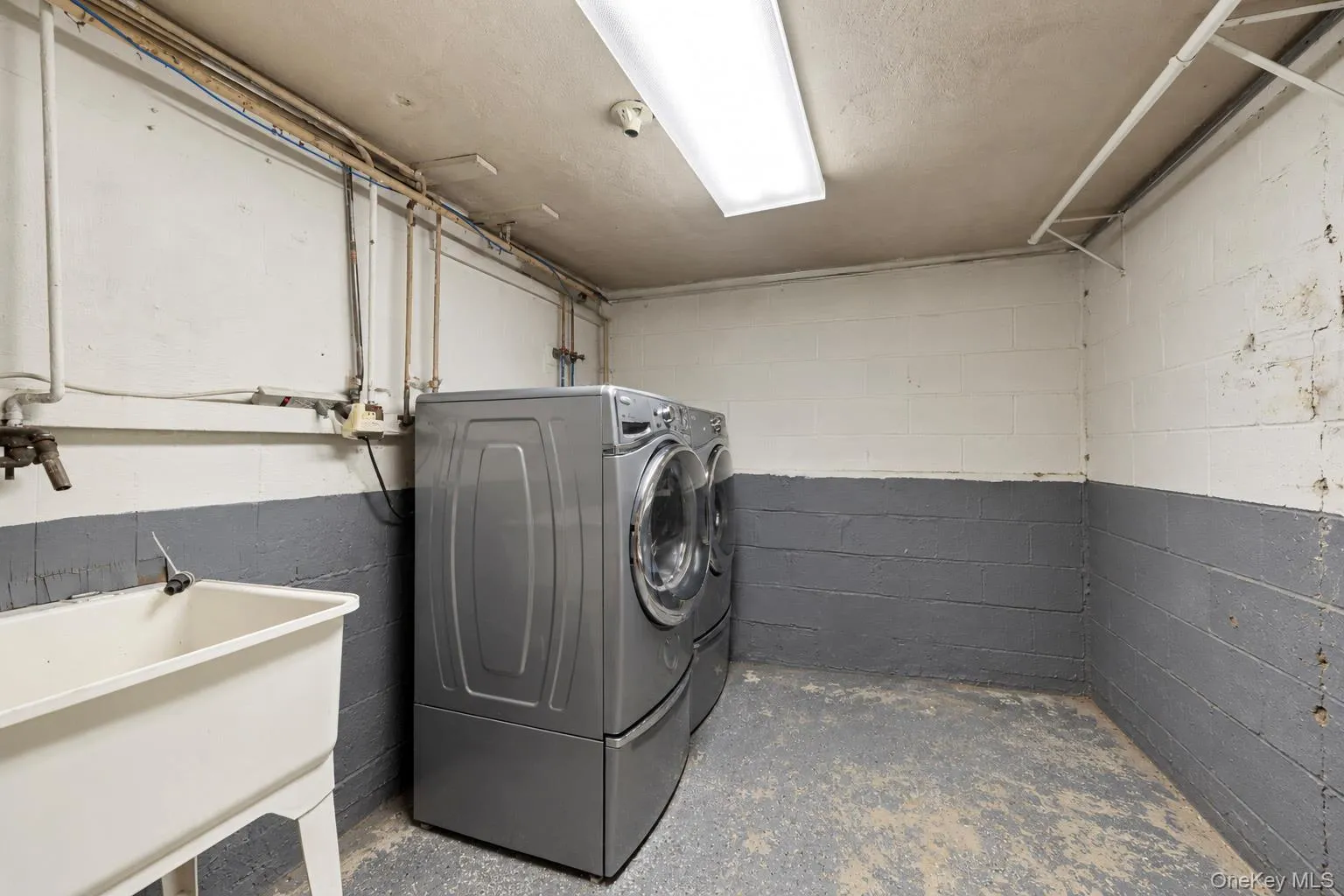 Utility space featuring a white utility sink, painted block walls, and overhead lighting Utility space featuring a white utility sink, painted block walls, and overhead lighting
