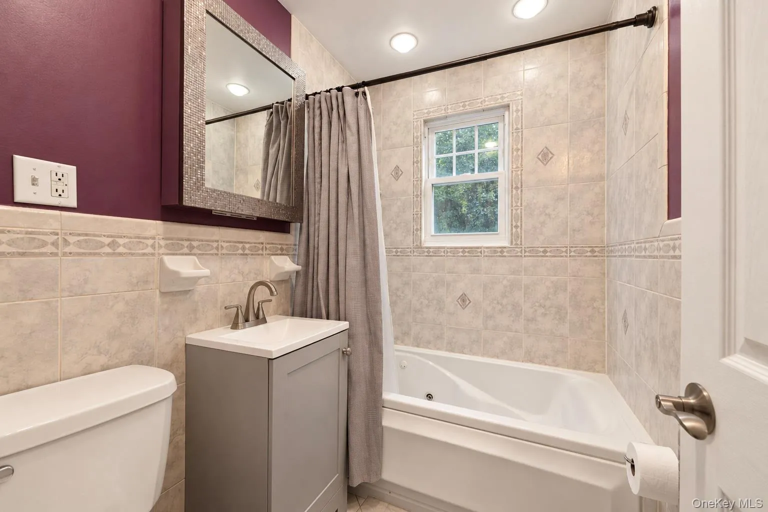 Bathroom featuring a jetted tub, tiled walls with decorative trim, vanity cabinet with a vessel-style sink, integrated recessed lighting, and a medicine cabinet with an textured frame Bathroom featuring a jetted tub, tiled walls with decorative trim, vanity cabinet with a vessel-style sink, integrated recessed lighting, and a medicine cabinet with an textured frame