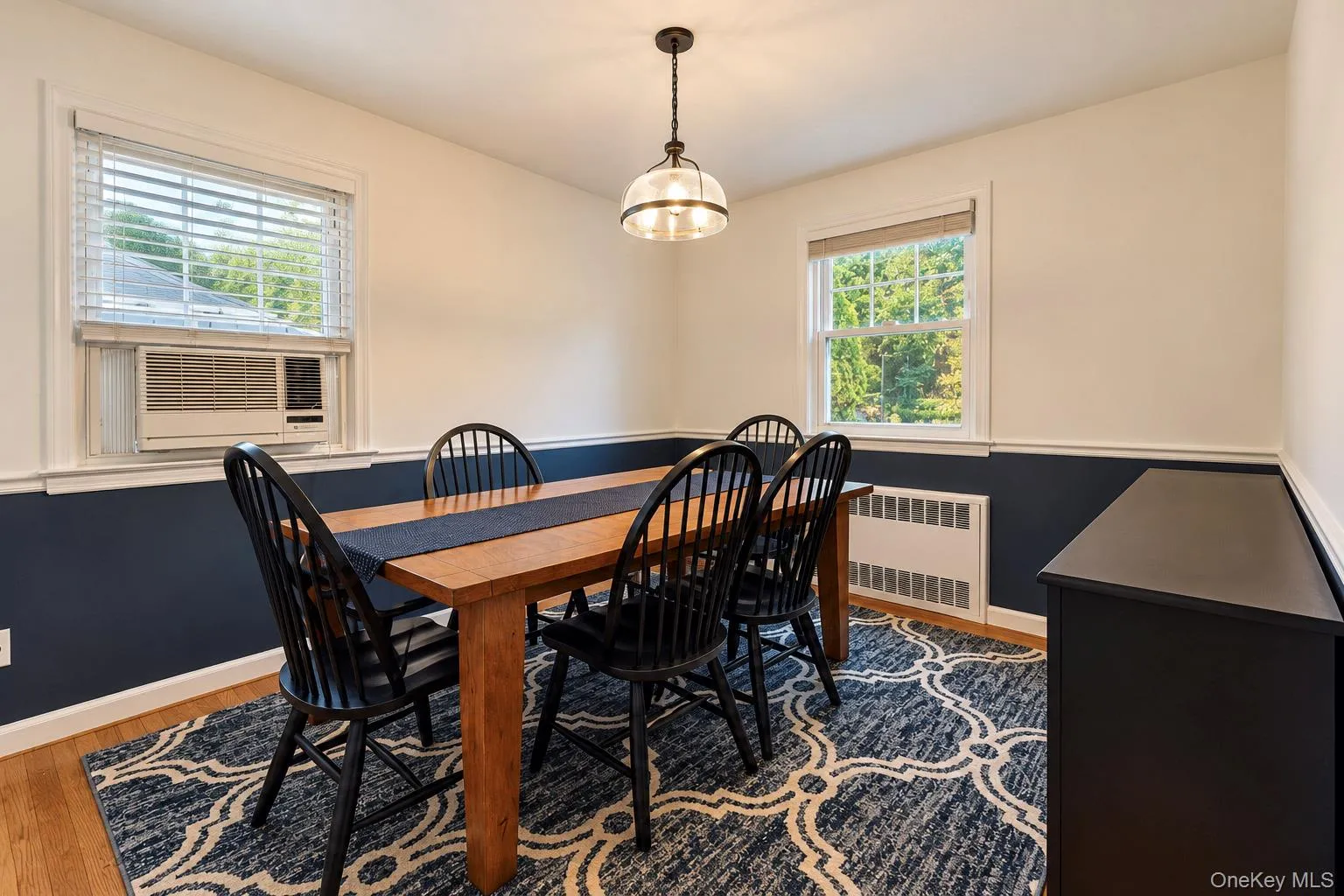 Interior space featuring two-tone wall paint, a central pendant light fixture, wood-finish flooring, and windows with white casings Interior space featuring two-tone wall paint, a central pendant light fixture, wood-finish flooring, and windows with white casings