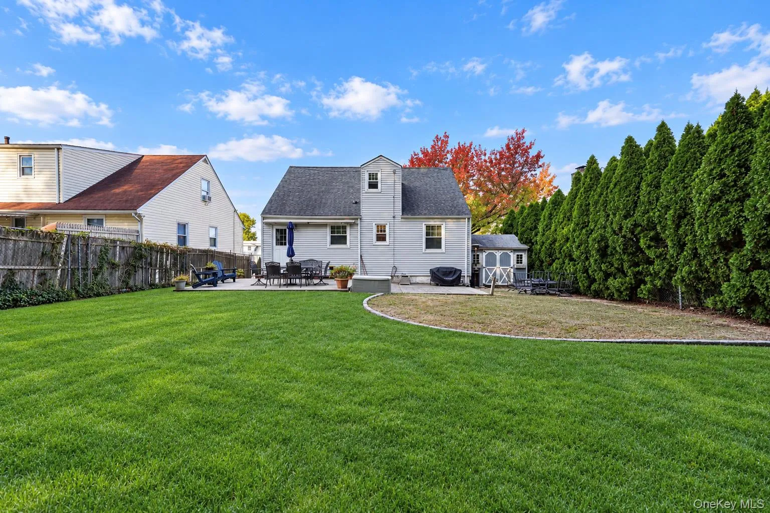 Expansive rear yard featuring a manicured lawn, stone patio, perimeter privacy hedging, and an exterior storage shed Expansive rear yard featuring a manicured lawn, stone patio, perimeter privacy hedging, and an exterior storage shed