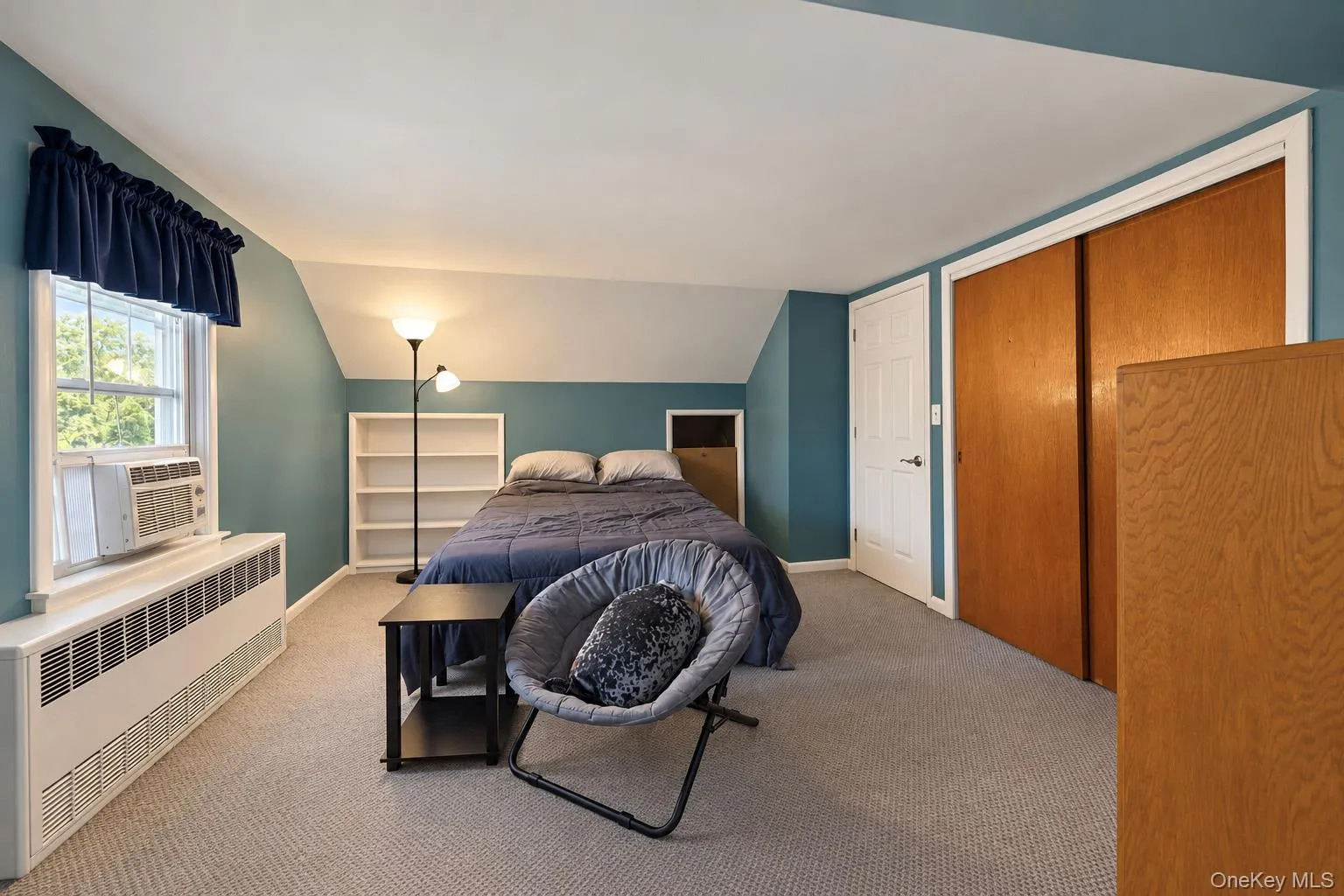 Interior space featuring sloped ceilings, integrated recessed shelving, wall-to-wall carpeting, and sliding wood-finish closet doors Interior space featuring sloped ceilings, integrated recessed shelving, wall-to-wall carpeting, and sliding wood-finish closet doors