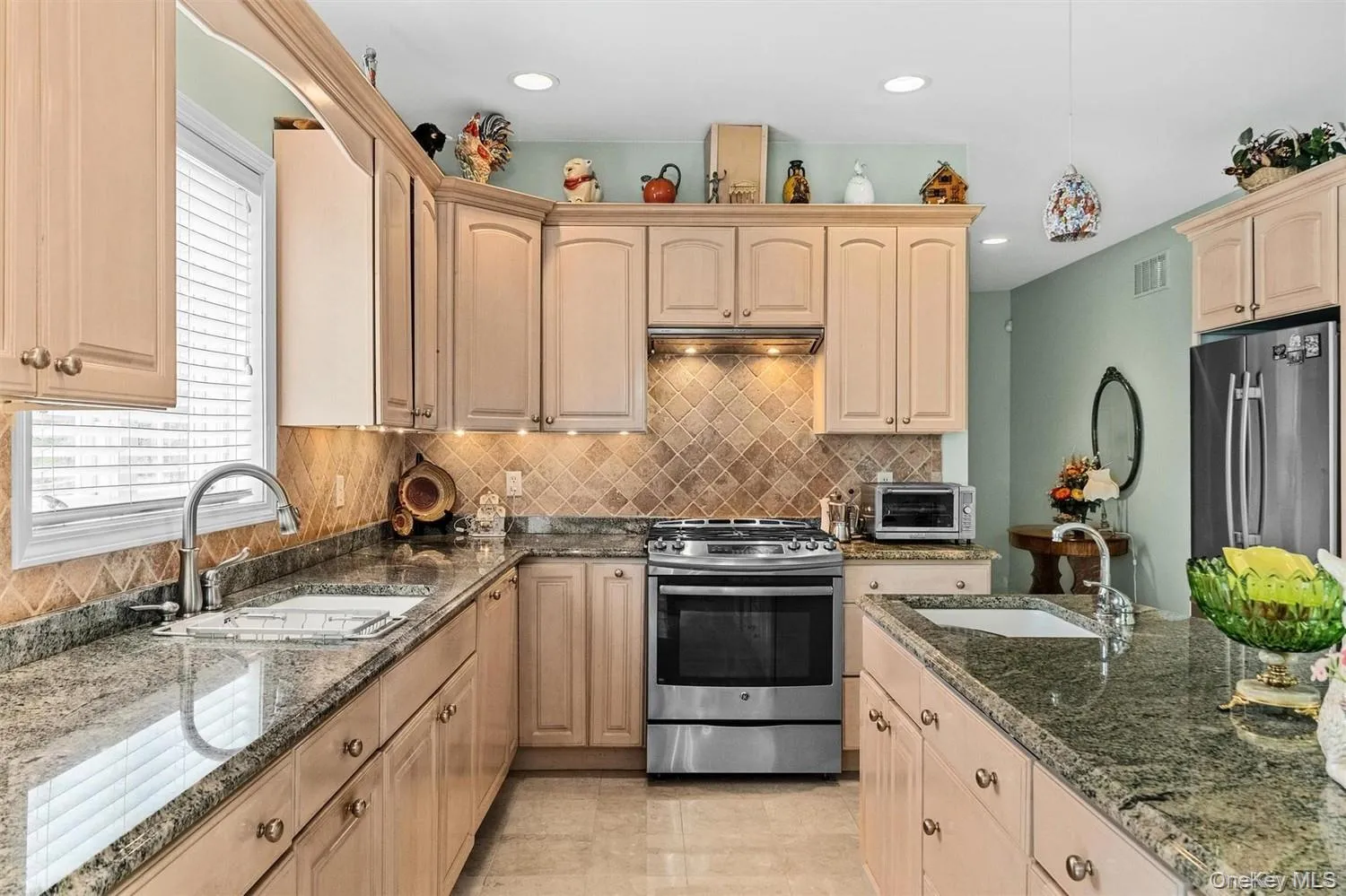 Kitchen with light wood finish cabinets, dark stone countertops, stainless steel appliances, and pendant lighting Kitchen with light wood finish cabinets, dark stone countertops, stainless steel appliances, and pendant lighting