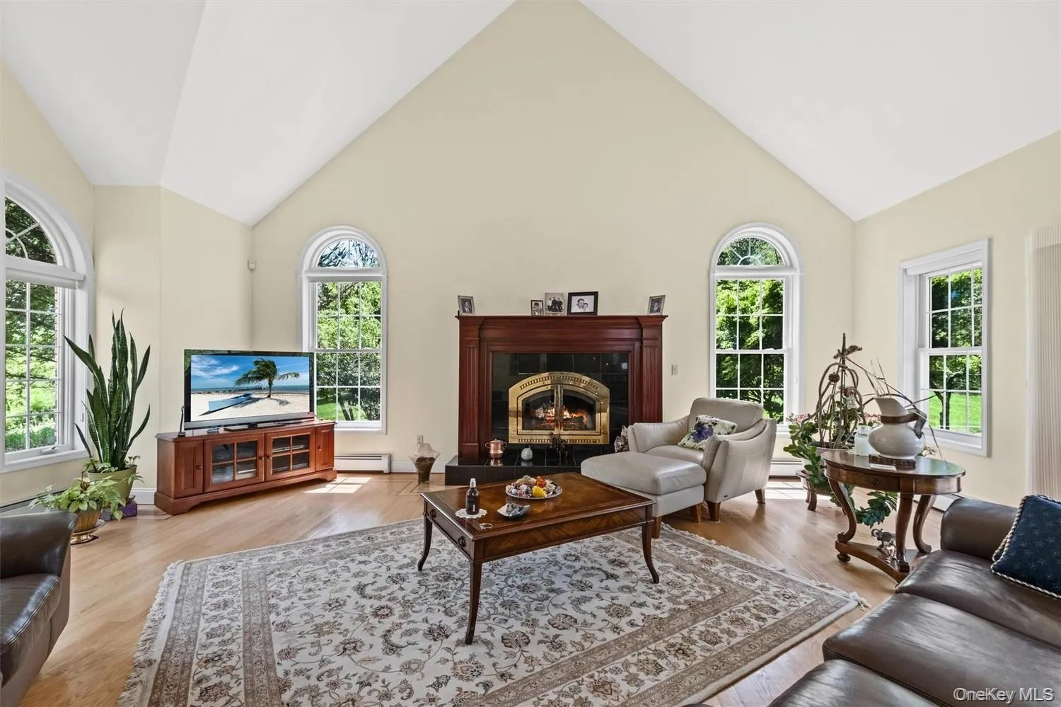Living room with a high ceiling, light wood finished floors, baseboard heating, and a high end fireplace Living room with a high ceiling, light wood finished floors, baseboard heating, and a high end fireplace