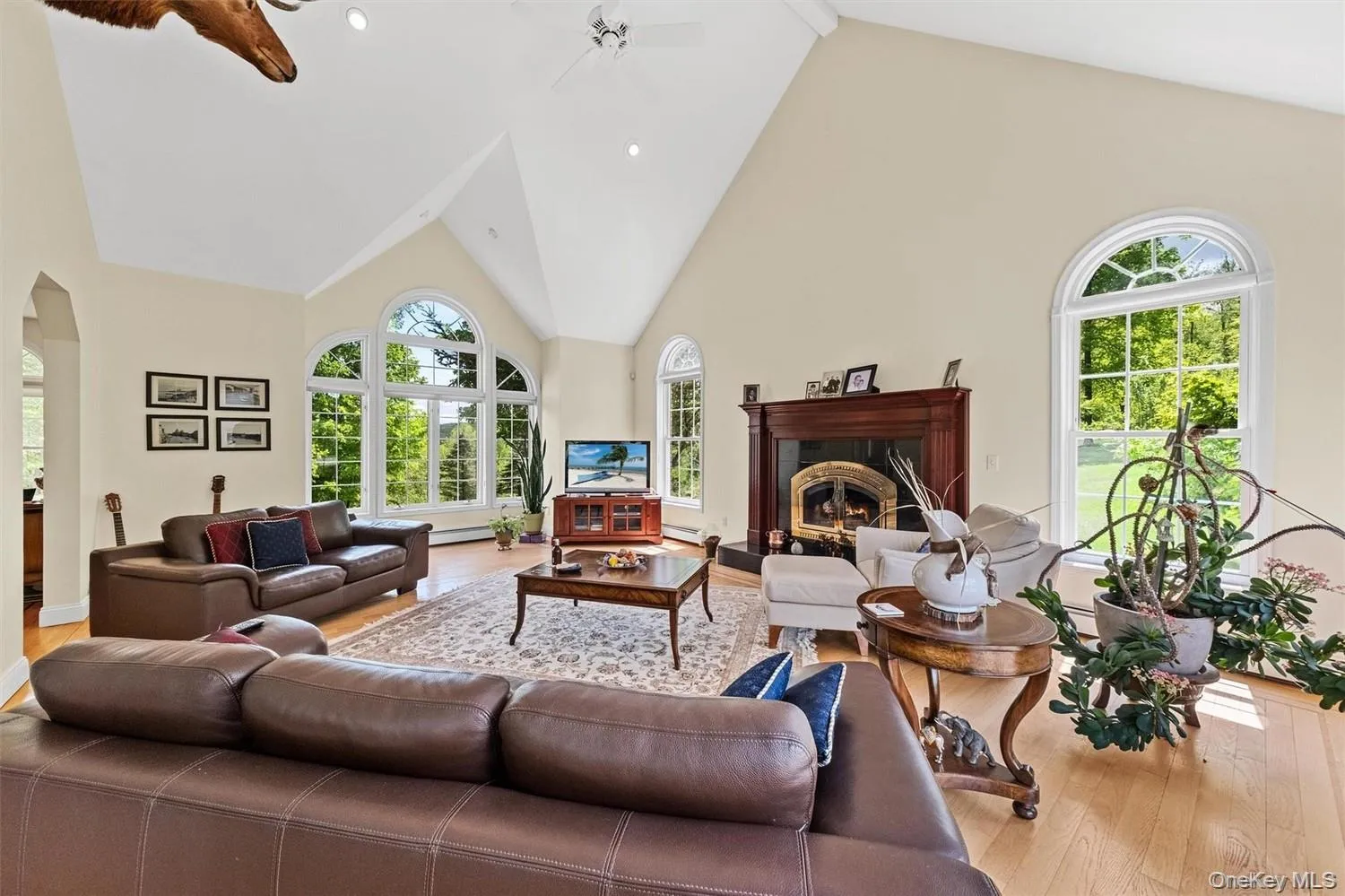 Living room with a high ceiling, light wood finished floors, a fireplace, ceiling fan, and arched walkways Living room with a high ceiling, light wood finished floors, a fireplace, ceiling fan, and arched walkways
