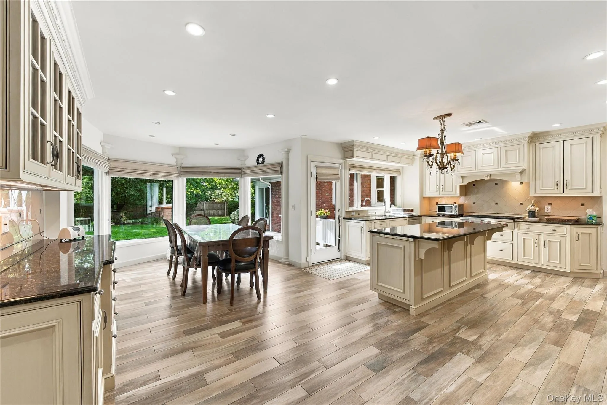 Kitchen featuring wood-finish flooring, custom cabinetry, central island with stone countertop, tile backsplash, and bay windows Kitchen featuring wood-finish flooring, custom cabinetry, central island with stone countertop, tile backsplash, and bay windows