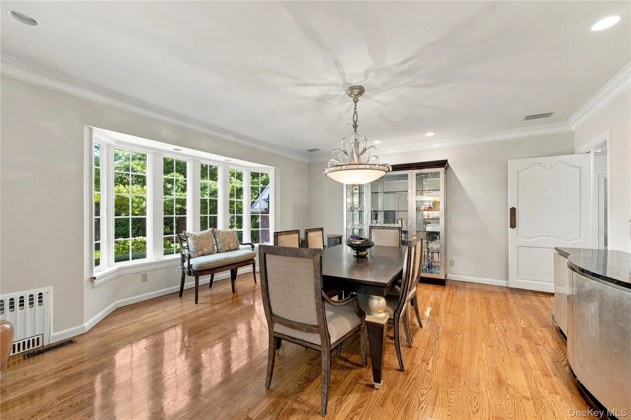 Dining area featuring wood-finish flooring, a multi-pane bay window, crown molding, and an overhead chandelier with crystal accents Dining area featuring wood-finish flooring, a multi-pane bay window, crown molding, and an overhead chandelier with crystal accents