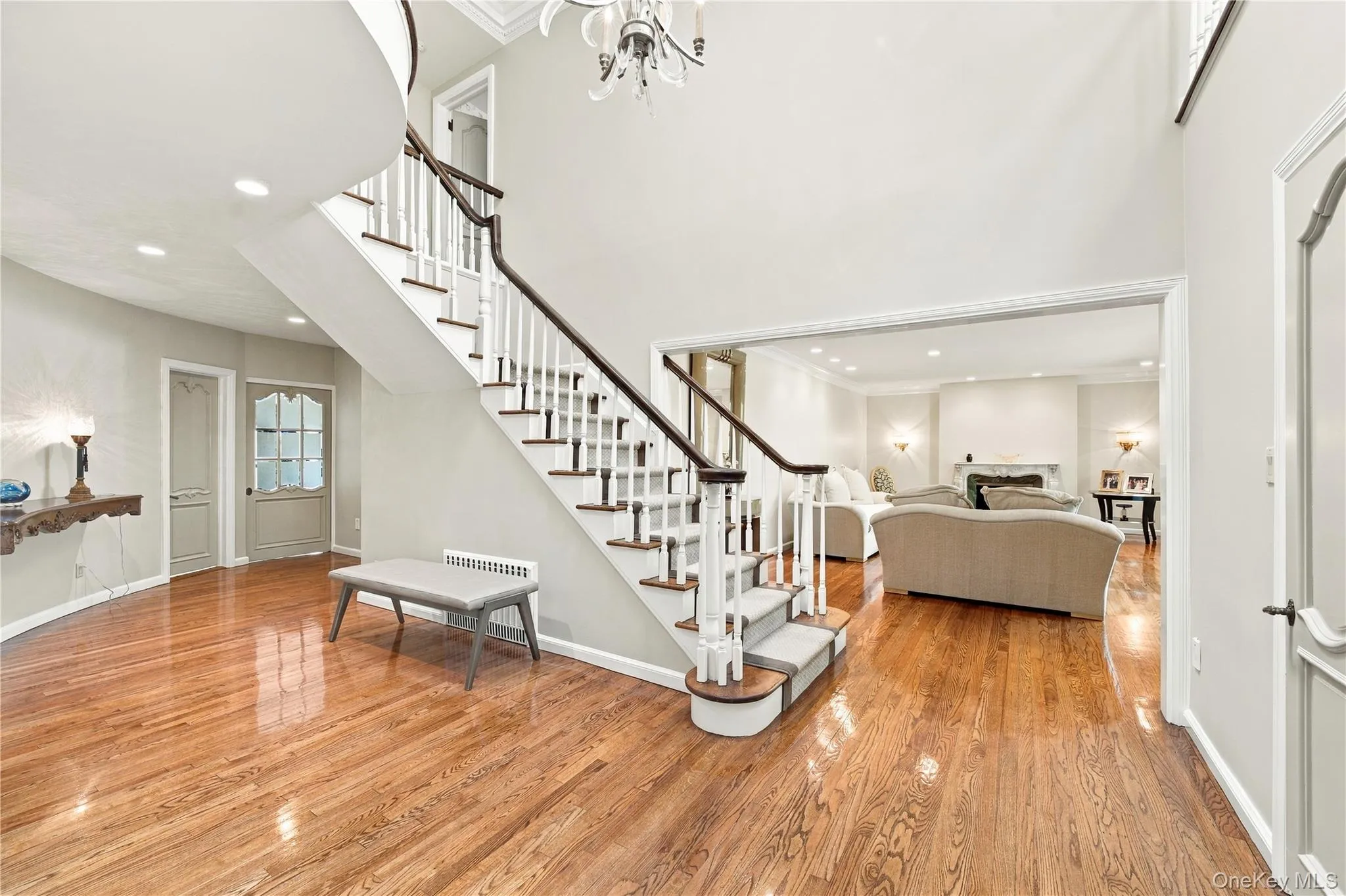 Foyer featuring wood-finish flooring, a two-story ceiling, a staircase with a white spindle railing, and overhead chandelier lighting Foyer featuring wood-finish flooring, a two-story ceiling, a staircase with a white spindle railing, and overhead chandelier lighting