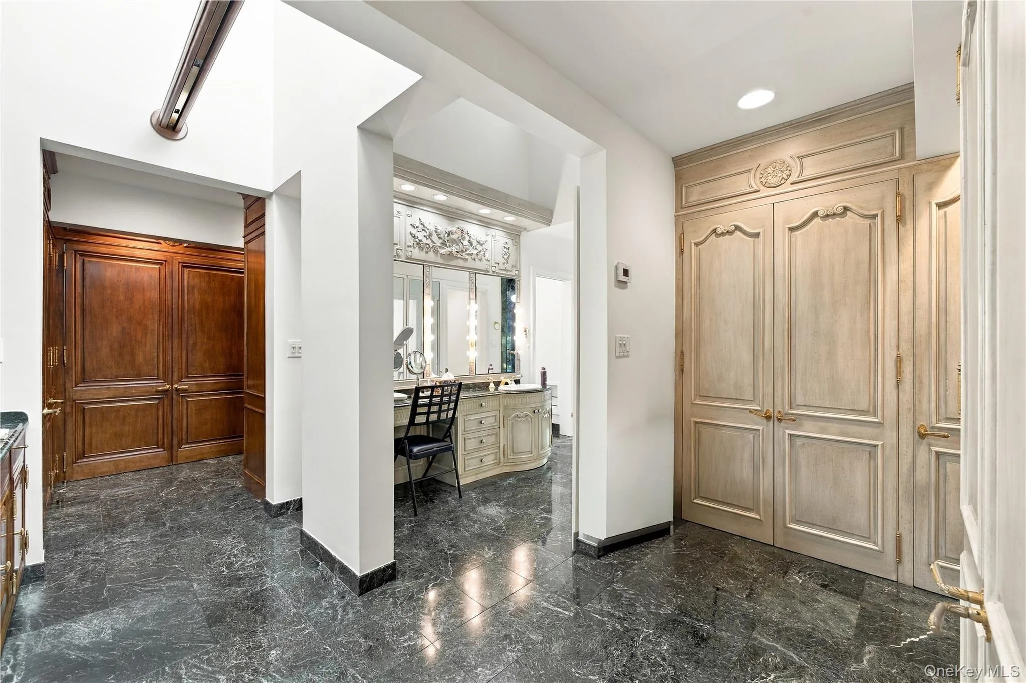 Polished stone flooring, custom floor-to-ceiling cabinetry with ornate detailing, built-in vanity with integrated lighting, and stained wood double doors Polished stone flooring, custom floor-to-ceiling cabinetry with ornate detailing, built-in vanity with integrated lighting, and stained wood double doors