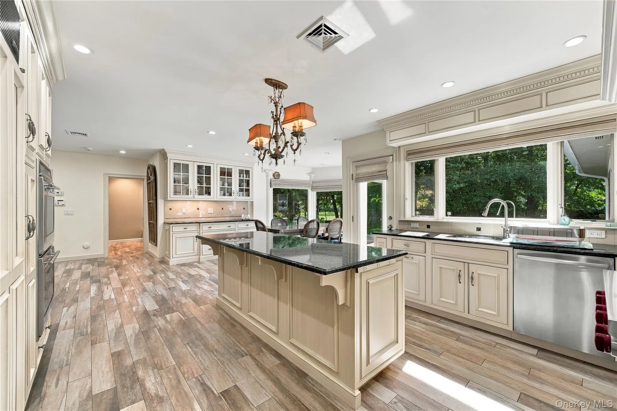 Kitchen featuring custom cabinetry with crown molding, a center island with a dark stone countertop, stainless steel appliances, wood-finish flooring, and recessed lighting Kitchen featuring custom cabinetry with crown molding, a center island with a dark stone countertop, stainless steel appliances, wood-finish flooring, and recessed lighting