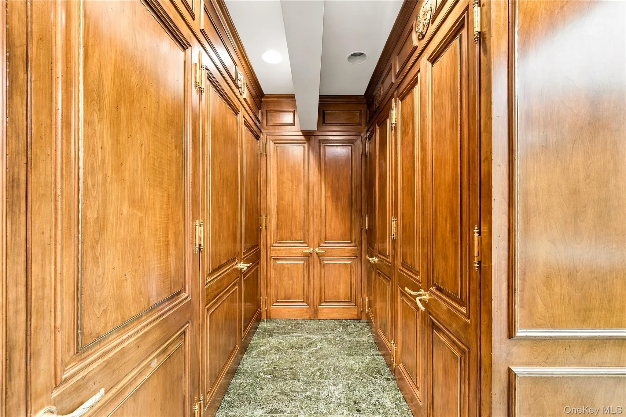 Floor-to-ceiling wood paneling featuring intricate raised-panel detailing, solid wood double doors, decorative brass hardware, and polished stone flooring Floor-to-ceiling wood paneling featuring intricate raised-panel detailing, solid wood double doors, decorative brass hardware, and polished stone flooring