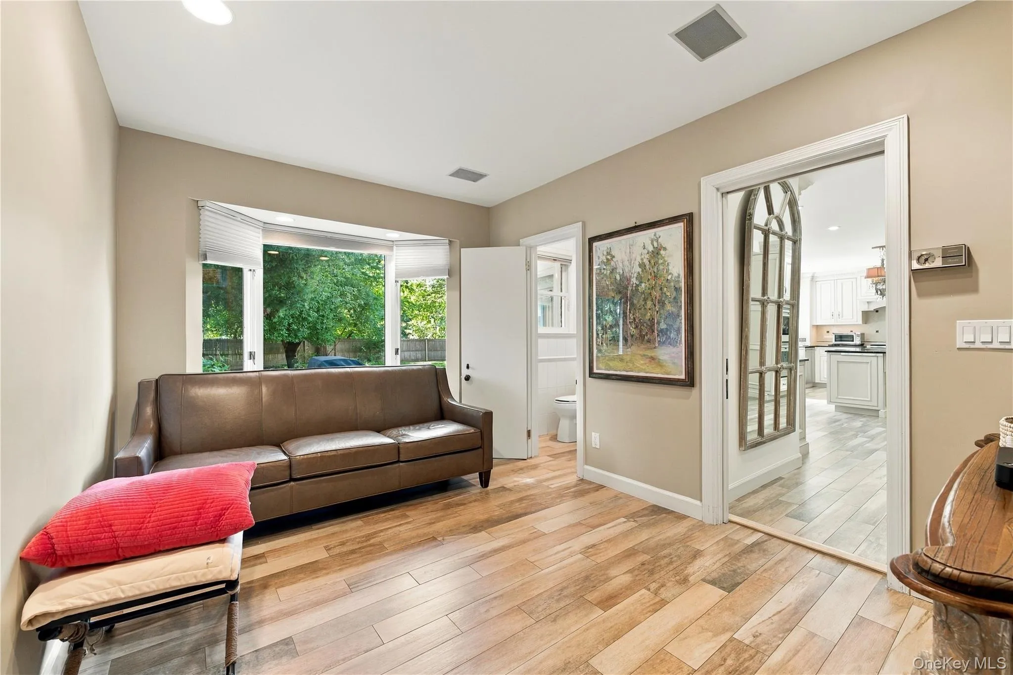 Room featuring wood-finish flooring, a large bay window, and a wide doorway opening to a secondary space Room featuring wood-finish flooring, a large bay window, and a wide doorway opening to a secondary space