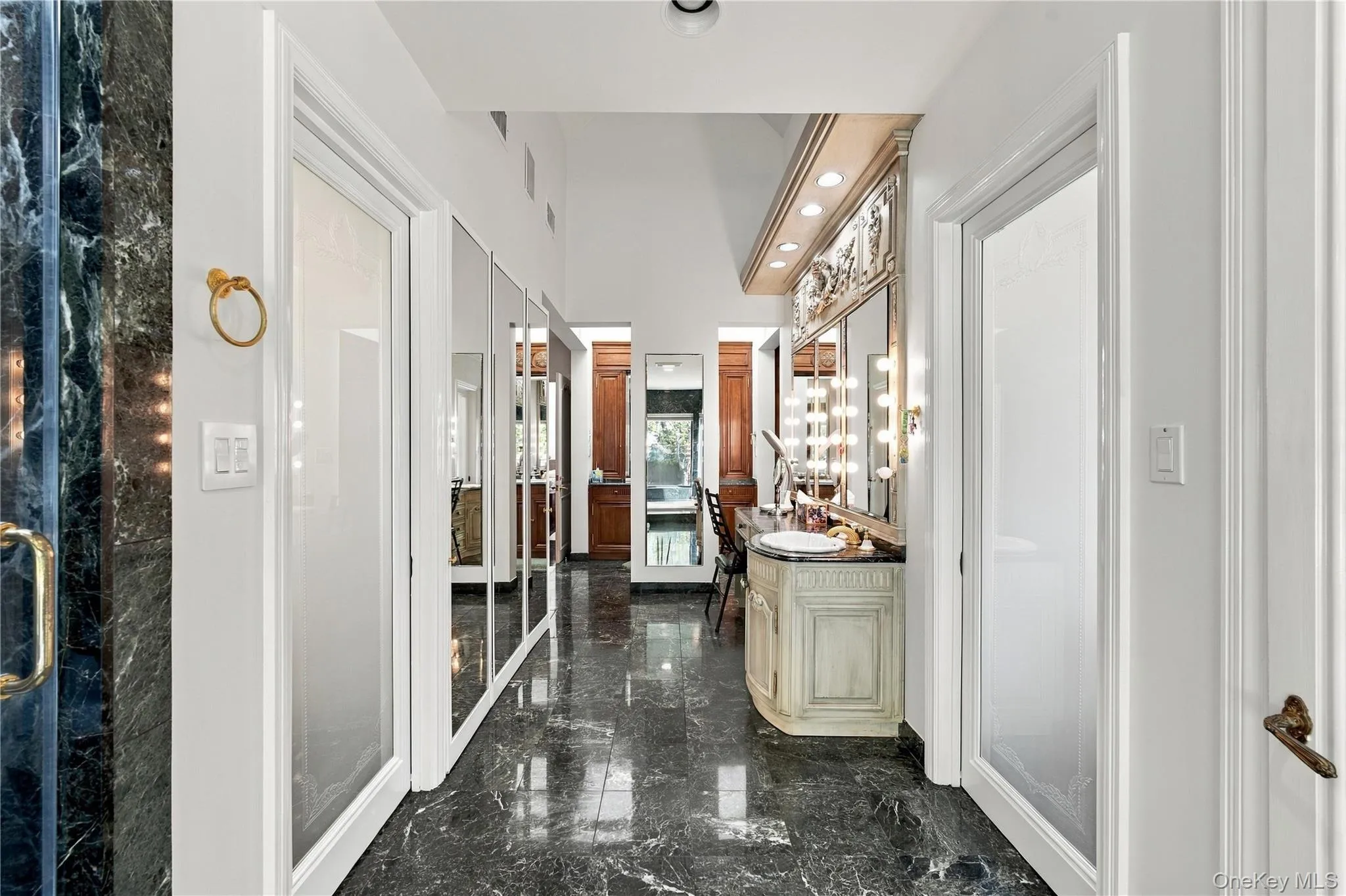 Polished stone flooring, built-in vanity with integrated lighting, full-length mirrored panels, and custom millwork featuring crown molding Polished stone flooring, built-in vanity with integrated lighting, full-length mirrored panels, and custom millwork featuring crown molding