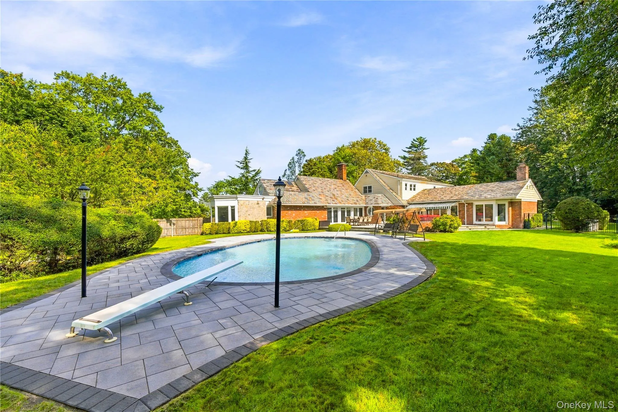 Backyard grounds featuring an inground swimming pool with a diving board, surrounding paver patio, and expansive lawn area Backyard grounds featuring an inground swimming pool with a diving board, surrounding paver patio, and expansive lawn area