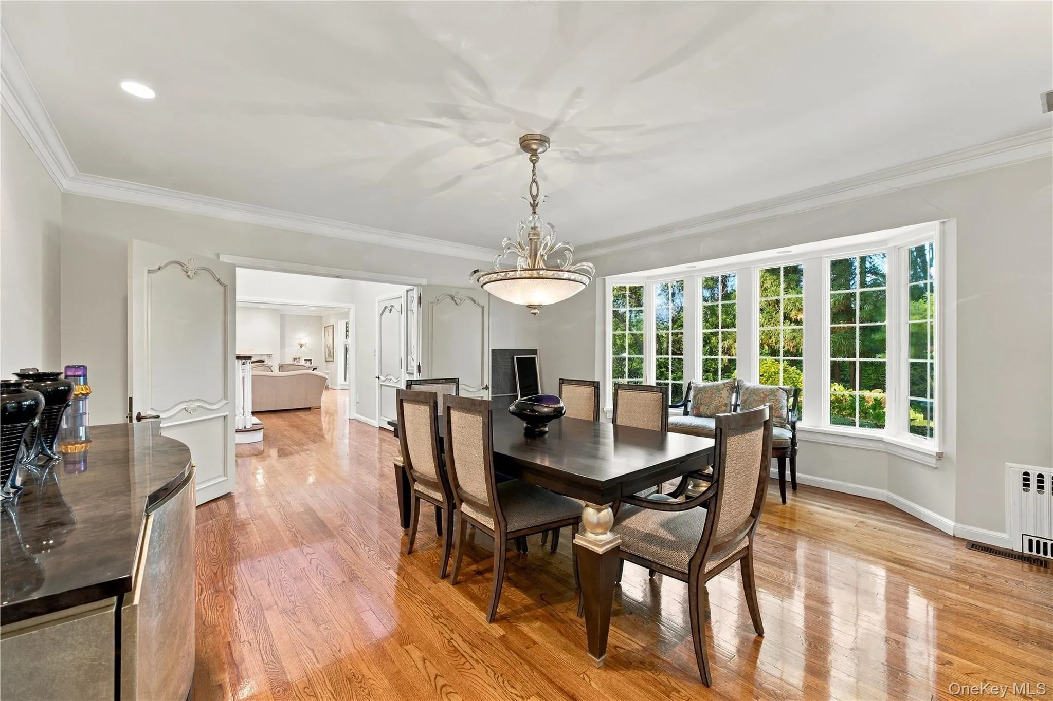 Dining area featuring wood-finish flooring, crown molding, an expansive bay window, and a decorative tiered chandelier Dining area featuring wood-finish flooring, crown molding, an expansive bay window, and a decorative tiered chandelier