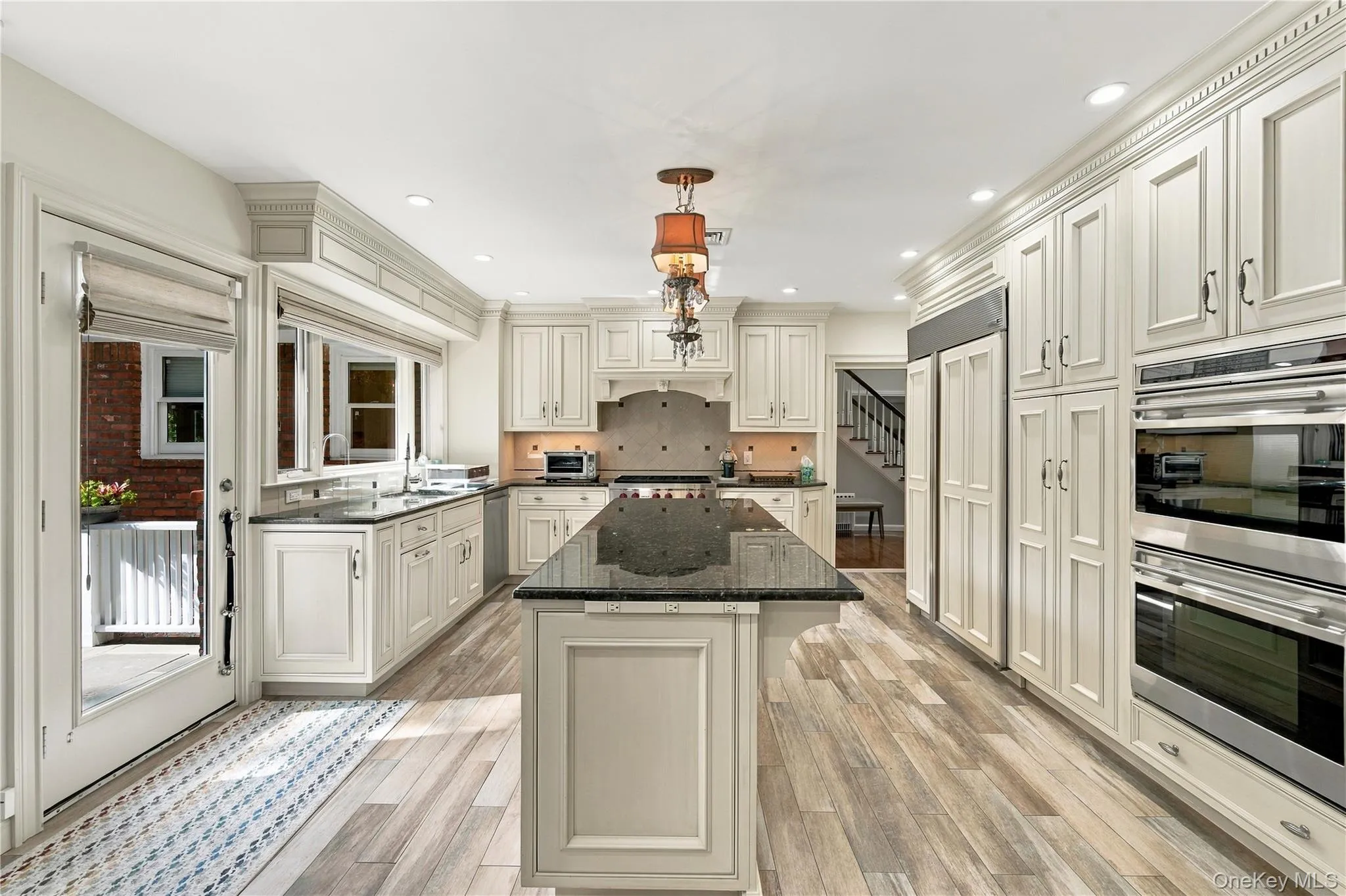 Kitchen featuring light-toned recessed-panel cabinetry, a central island with stone-finish countertops, stainless steel double wall ovens, wood-finish flooring, and recessed ceiling lighting Kitchen featuring light-toned recessed-panel cabinetry, a central island with stone-finish countertops, stainless steel double wall ovens, wood-finish flooring, and recessed ceiling lighting
