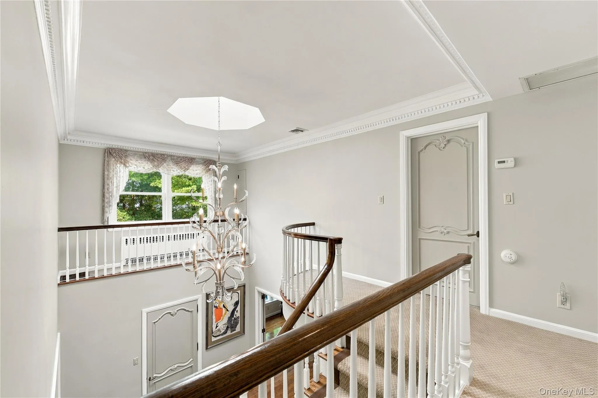 Open landing featuring tiered crown molding, a decorative metal chandelier, arched-panel interior doors, and a curved staircase with a wood handrail Open landing featuring tiered crown molding, a decorative metal chandelier, arched-panel interior doors, and a curved staircase with a wood handrail