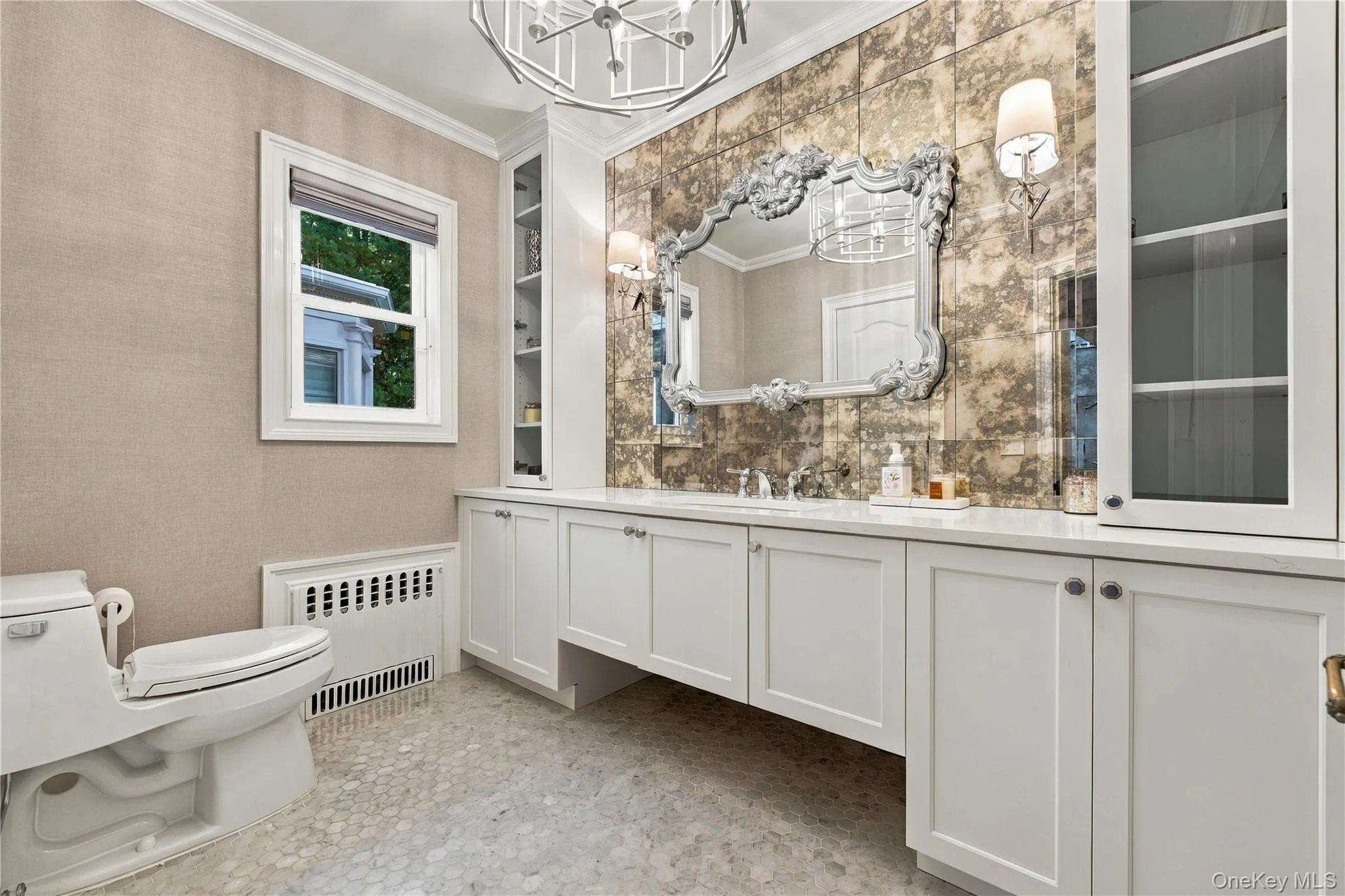 Custom white cabinetry with integrated storage, antique-style mirrored backsplash, metallic light fixtures, and stone-tiled flooring Custom white cabinetry with integrated storage, antique-style mirrored backsplash, metallic light fixtures, and stone-tiled flooring