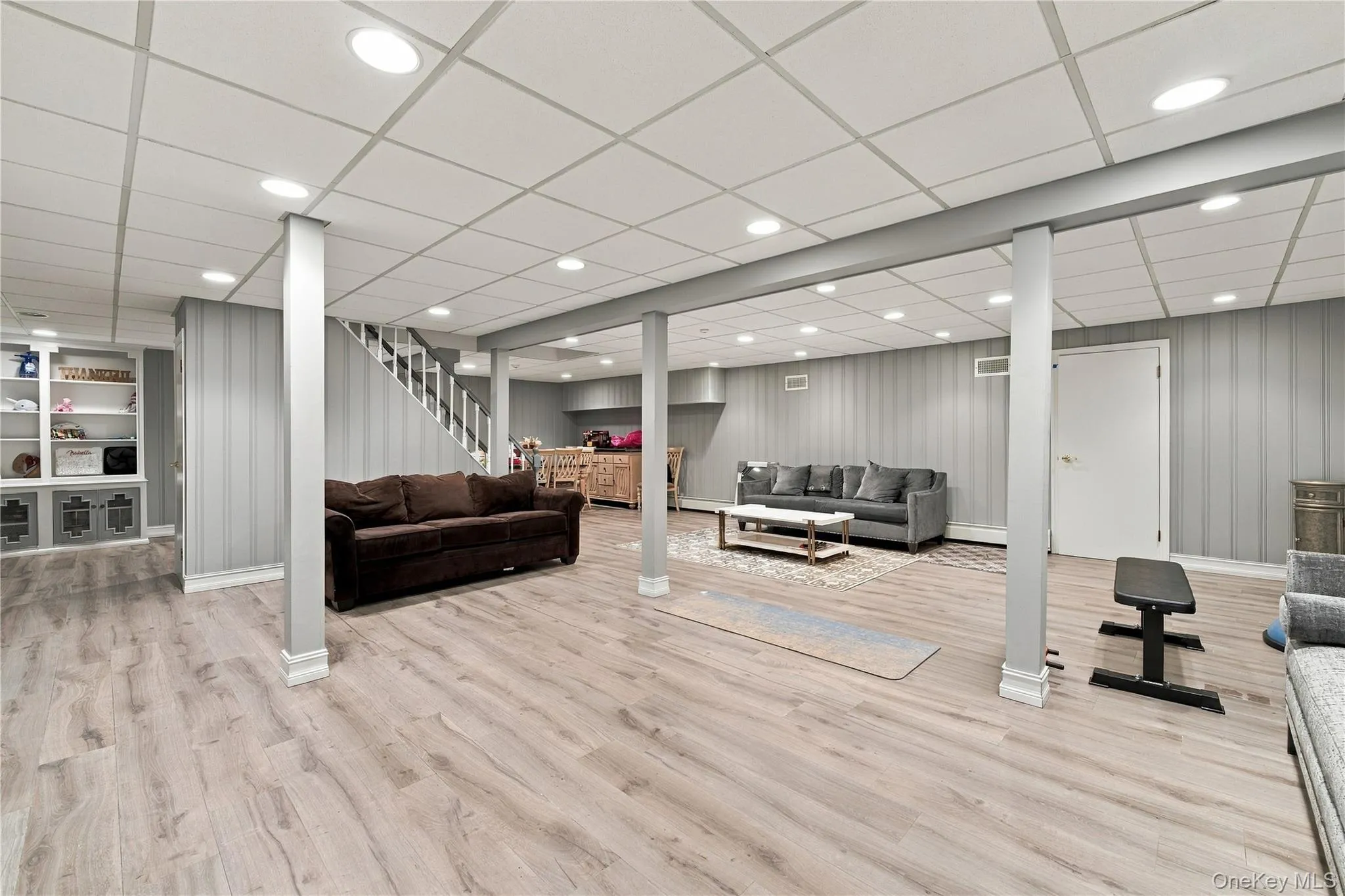 Finished lower level featuring wood-finish flooring, recessed lighting, drop ceiling, vertical paneling, and built-in shelving Finished lower level featuring wood-finish flooring, recessed lighting, drop ceiling, vertical paneling, and built-in shelving