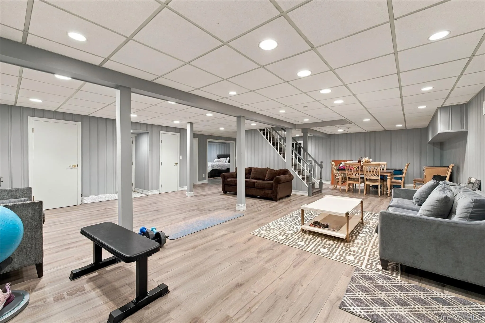 Finished lower level with wood-finish flooring, recessed lighting, vertical paneling, and a staircase featuring wood railings Finished lower level with wood-finish flooring, recessed lighting, vertical paneling, and a staircase featuring wood railings