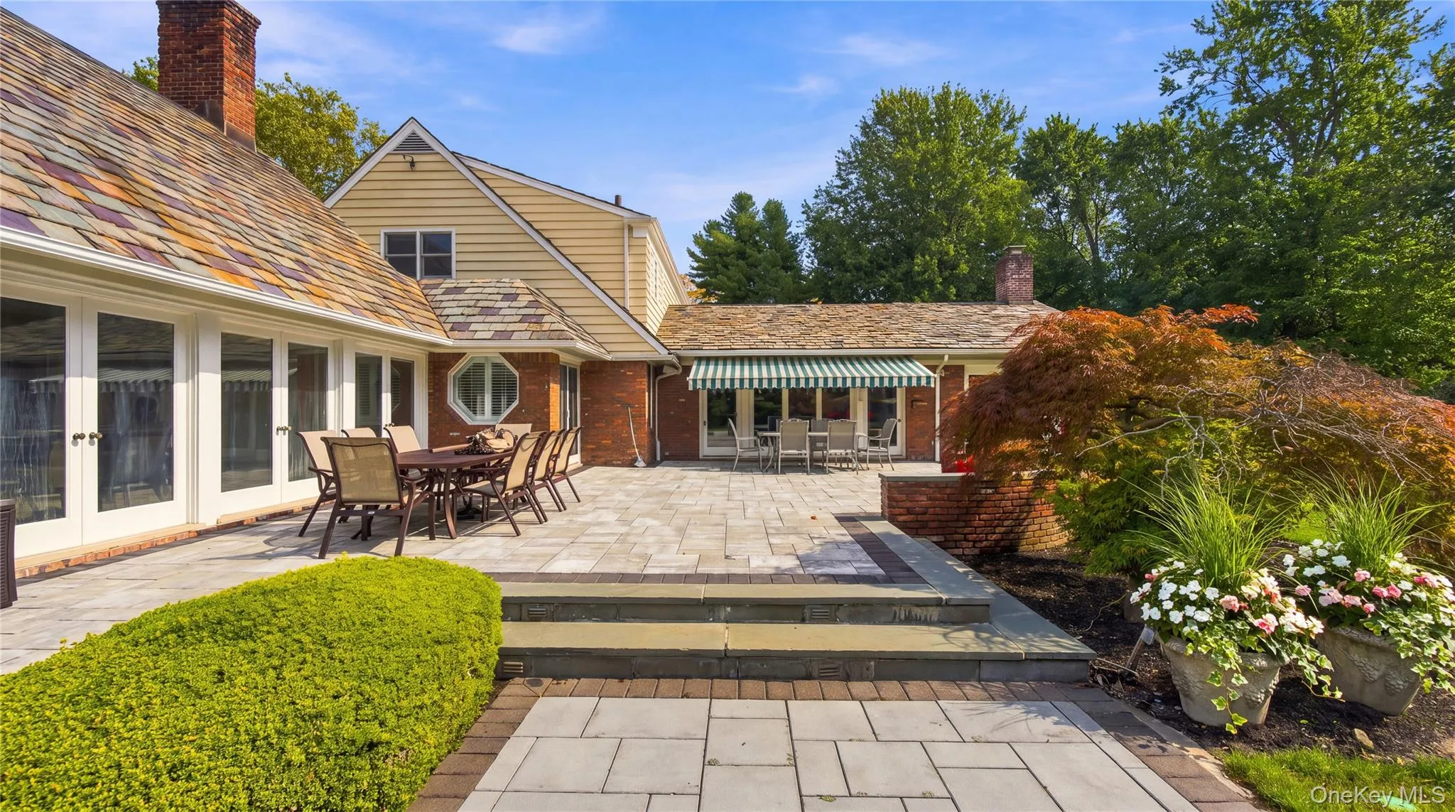Expansive stone patio featuring a multi-level terrace, brick retaining wall, retractable fabric awning, and slate-style shingle roof Expansive stone patio featuring a multi-level terrace, brick retaining wall, retractable fabric awning, and slate-style shingle roof