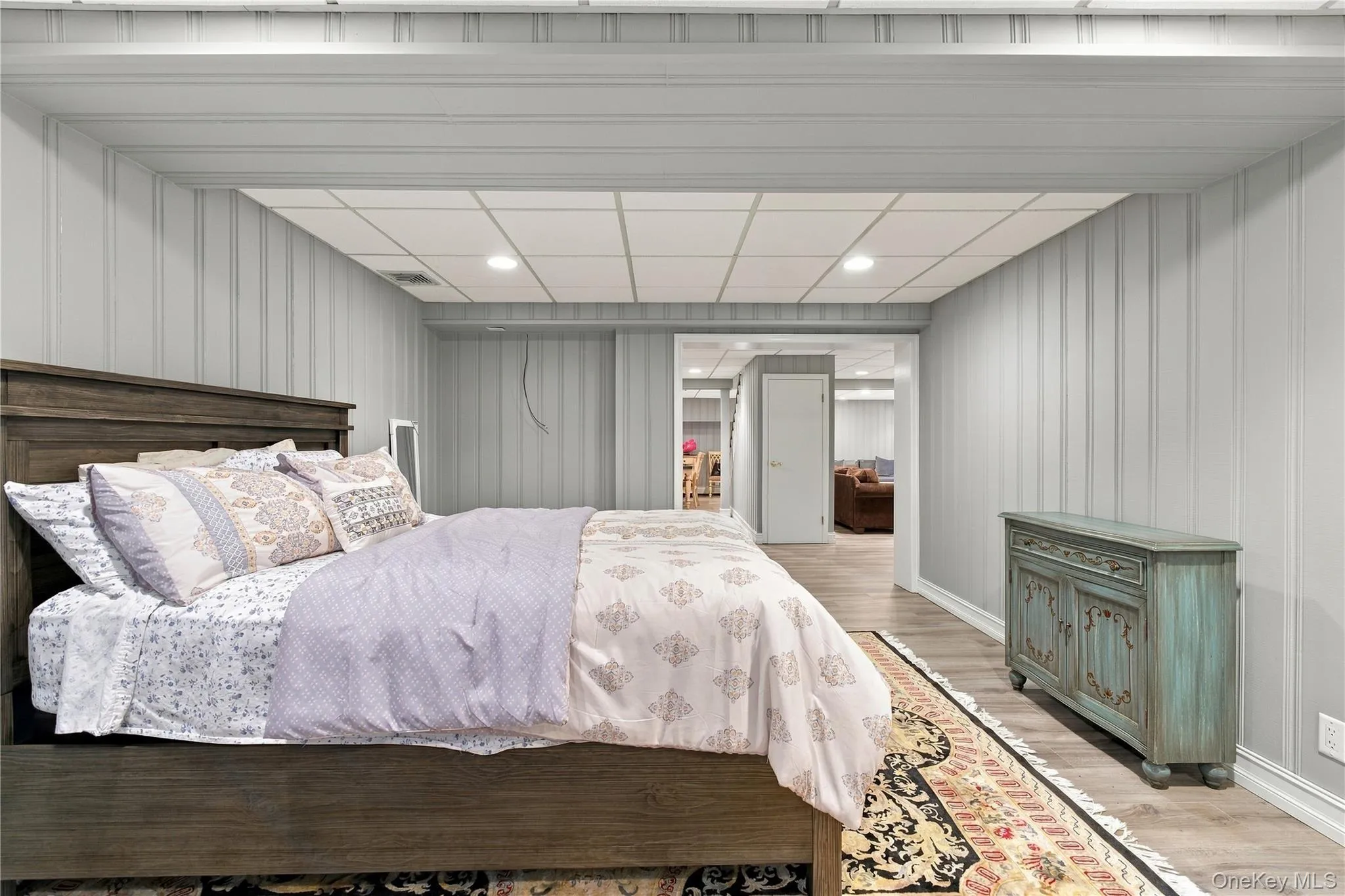 Finished room featuring vertical paneled walls, recessed ceiling lighting, a drop-ceiling grid, and wood-finish flooring Finished room featuring vertical paneled walls, recessed ceiling lighting, a drop-ceiling grid, and wood-finish flooring