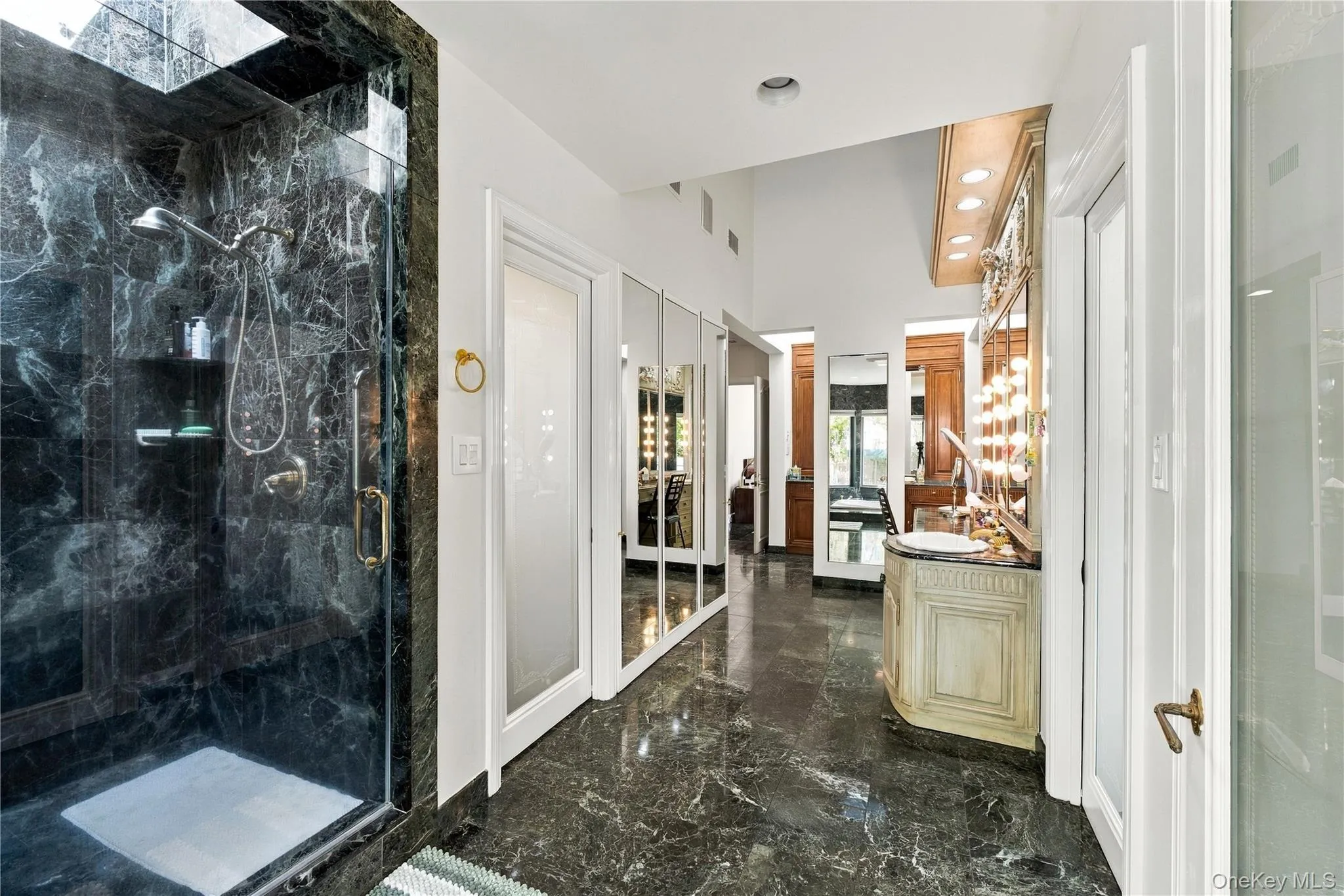 Enclosed shower featuring dark stone tile surround, stone flooring, built-in vanity with integrated lighting, recessed ceiling lighting, and floor-to-ceiling mirrored cabinetry Enclosed shower featuring dark stone tile surround, stone flooring, built-in vanity with integrated lighting, recessed ceiling lighting, and floor-to-ceiling mirrored cabinetry