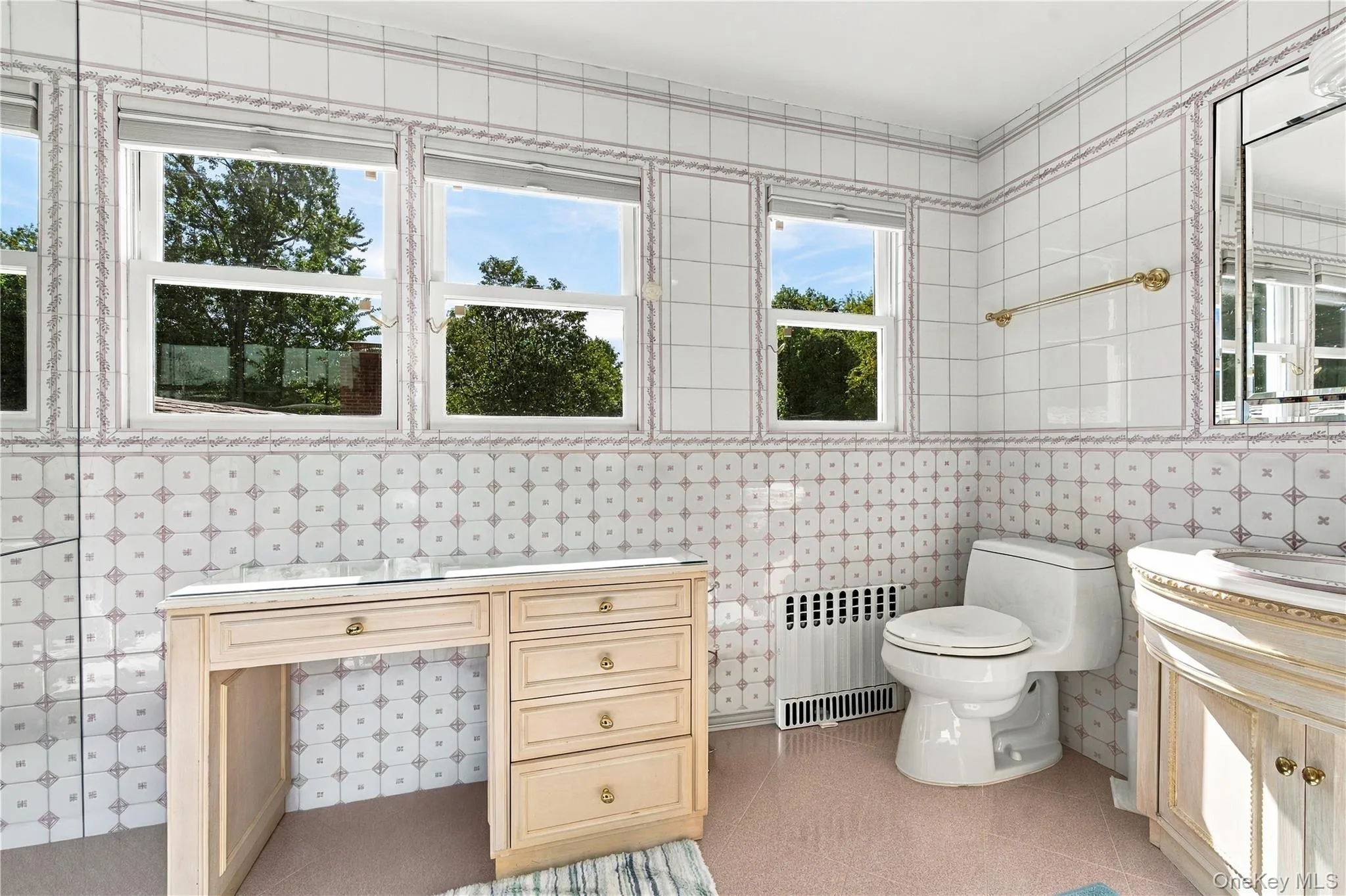 Bathroom featuring floor-to-ceiling decorative tile walls, built-in vanity cabinetry, and three large windows Bathroom featuring floor-to-ceiling decorative tile walls, built-in vanity cabinetry, and three large windows