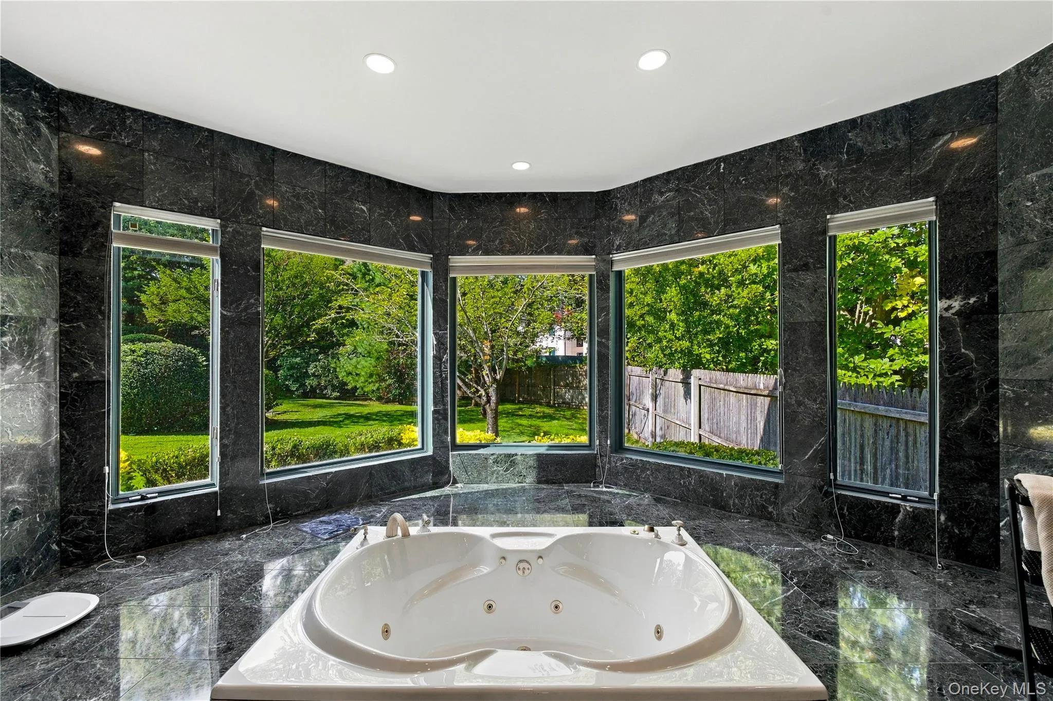 Polished stone wall and floor tiling, expansive multi-panel window configuration, and recessed soaking tub with integrated fixtures Polished stone wall and floor tiling, expansive multi-panel window configuration, and recessed soaking tub with integrated fixtures