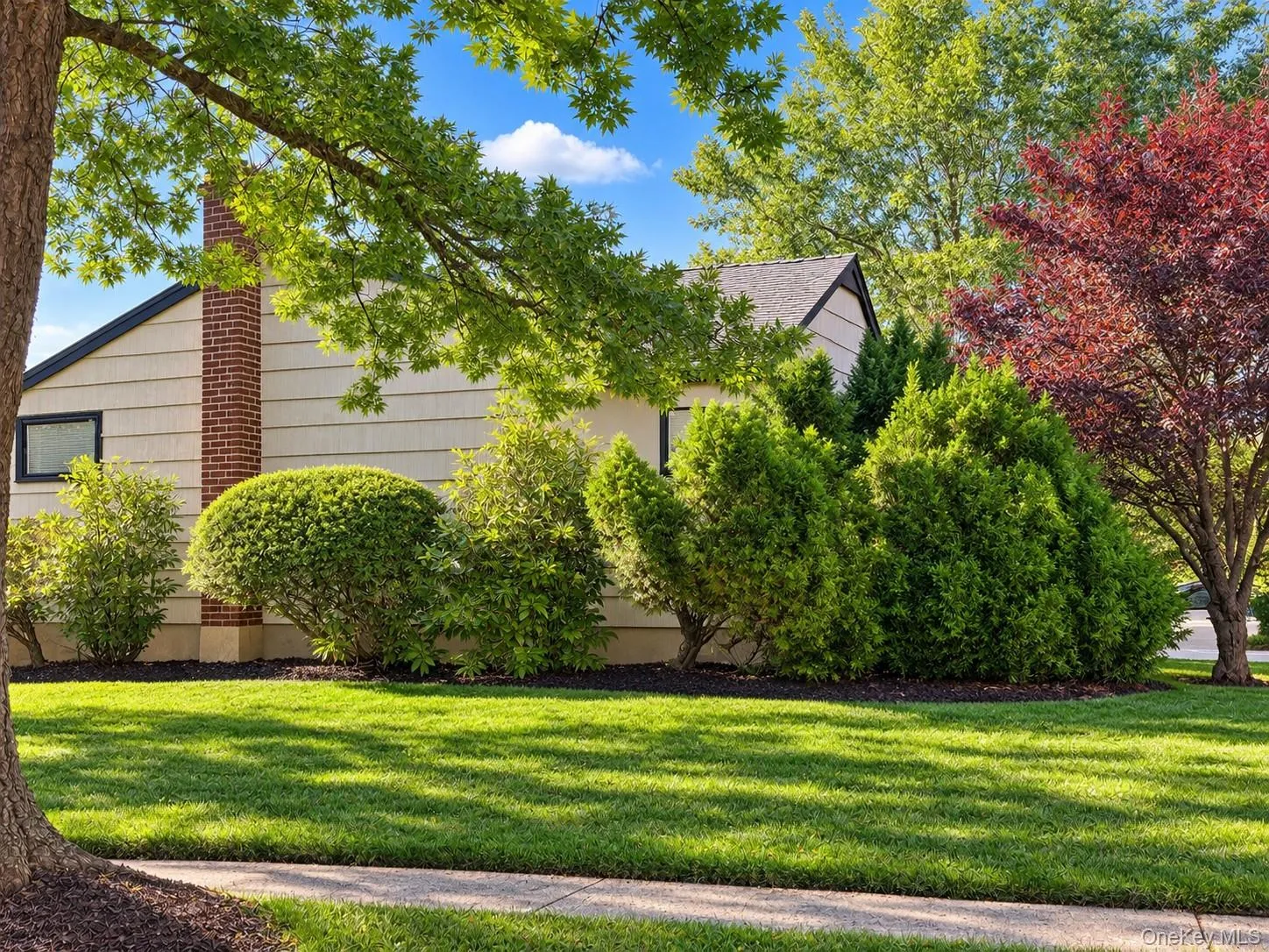 Manicured lawn, mature trees, and established shrubbery complement the exterior siding and brick chimney Manicured lawn, mature trees, and established shrubbery complement the exterior siding and brick chimney