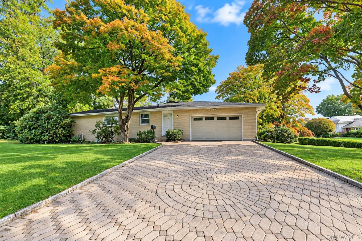 Single-story brick exterior featuring a patterned paver driveway, attached two-car garage, and established landscaping Single-story brick exterior featuring a patterned paver driveway, attached two-car garage, and established landscaping