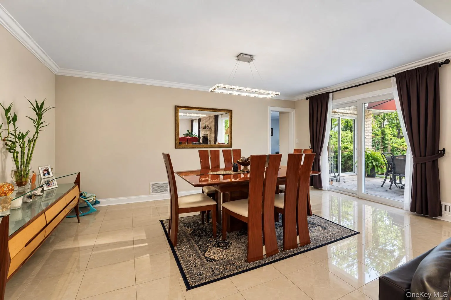 Dining area featuring polished large-format floor tiles, crown molding, a modern linear chandelier, and sliding glass doors to the exterior Dining area featuring polished large-format floor tiles, crown molding, a modern linear chandelier, and sliding glass doors to the exterior