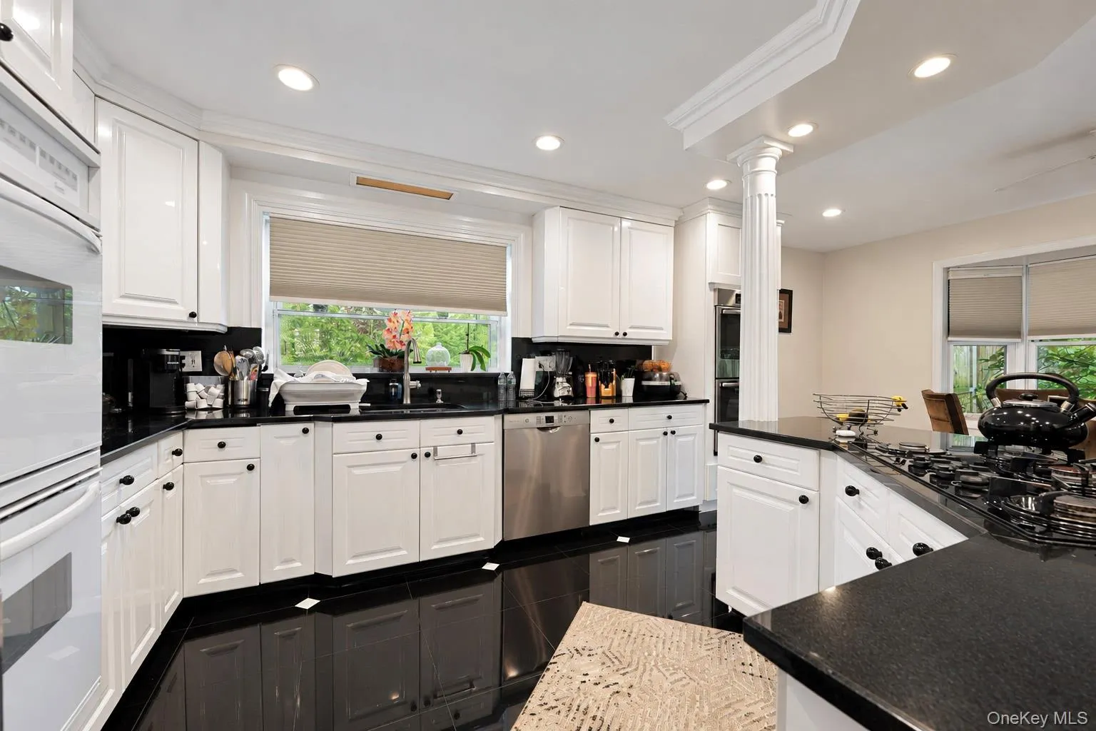 Kitchen featuring white cabinetry, dark stone countertops, stainless steel appliances, recessed ceiling lighting, and a decorative column Kitchen featuring white cabinetry, dark stone countertops, stainless steel appliances, recessed ceiling lighting, and a decorative column
