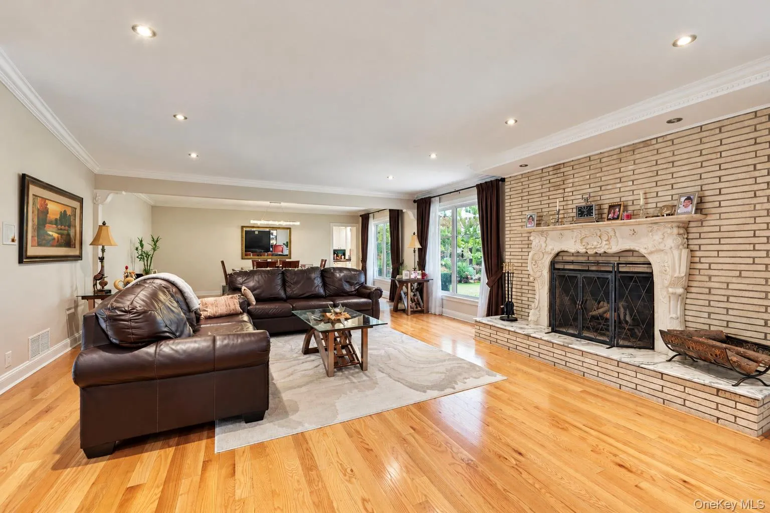 Living area featuring wood-finish flooring, recessed lighting, crown molding, and a floor-to-ceiling brick fireplace with an ornate stone mantel Living area featuring wood-finish flooring, recessed lighting, crown molding, and a floor-to-ceiling brick fireplace with an ornate stone mantel