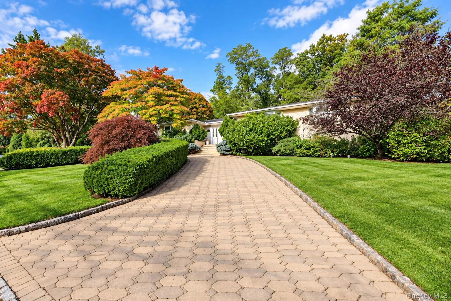 Stone paver driveway with Belgian block curbing, flanked by manicured lawns, shaped shrubbery, and mature deciduous trees Stone paver driveway with Belgian block curbing, flanked by manicured lawns, shaped shrubbery, and mature deciduous trees