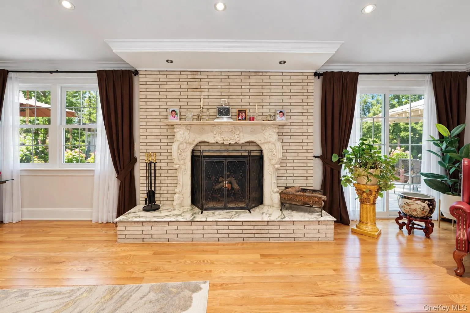 Light-toned brick fireplace with an ornate carved mantel and stone hearth, wood-finish flooring, recessed lighting, and glass paneled doors Light-toned brick fireplace with an ornate carved mantel and stone hearth, wood-finish flooring, recessed lighting, and glass paneled doors