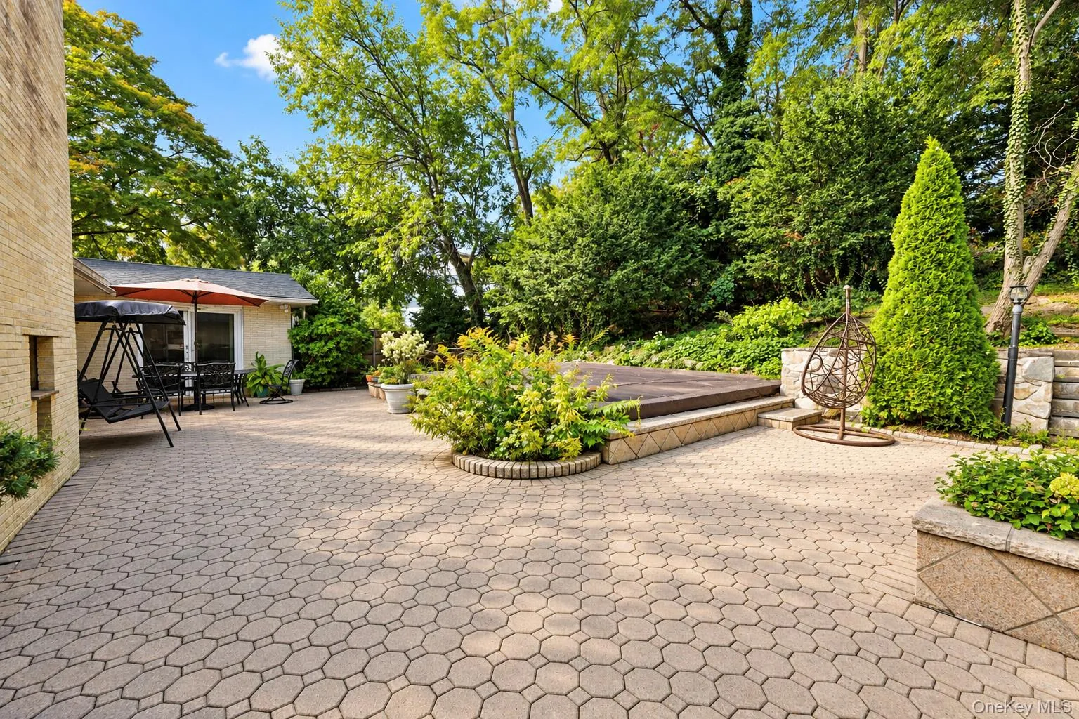 Expansive stone-paver patio featuring a built-in spa, tiered retaining walls, and mature landscaping Expansive stone-paver patio featuring a built-in spa, tiered retaining walls, and mature landscaping