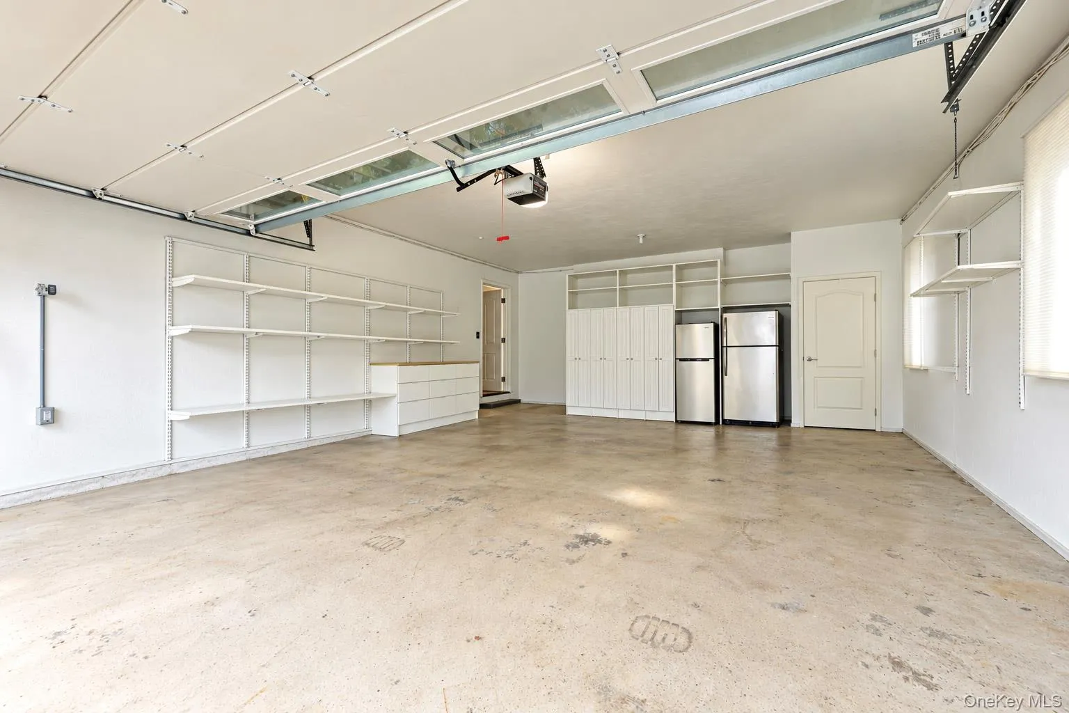 Multi-car garage featuring a concrete floor, integrated wall shelving, built-in cabinetry, and overhead lighting Multi-car garage featuring a concrete floor, integrated wall shelving, built-in cabinetry, and overhead lighting