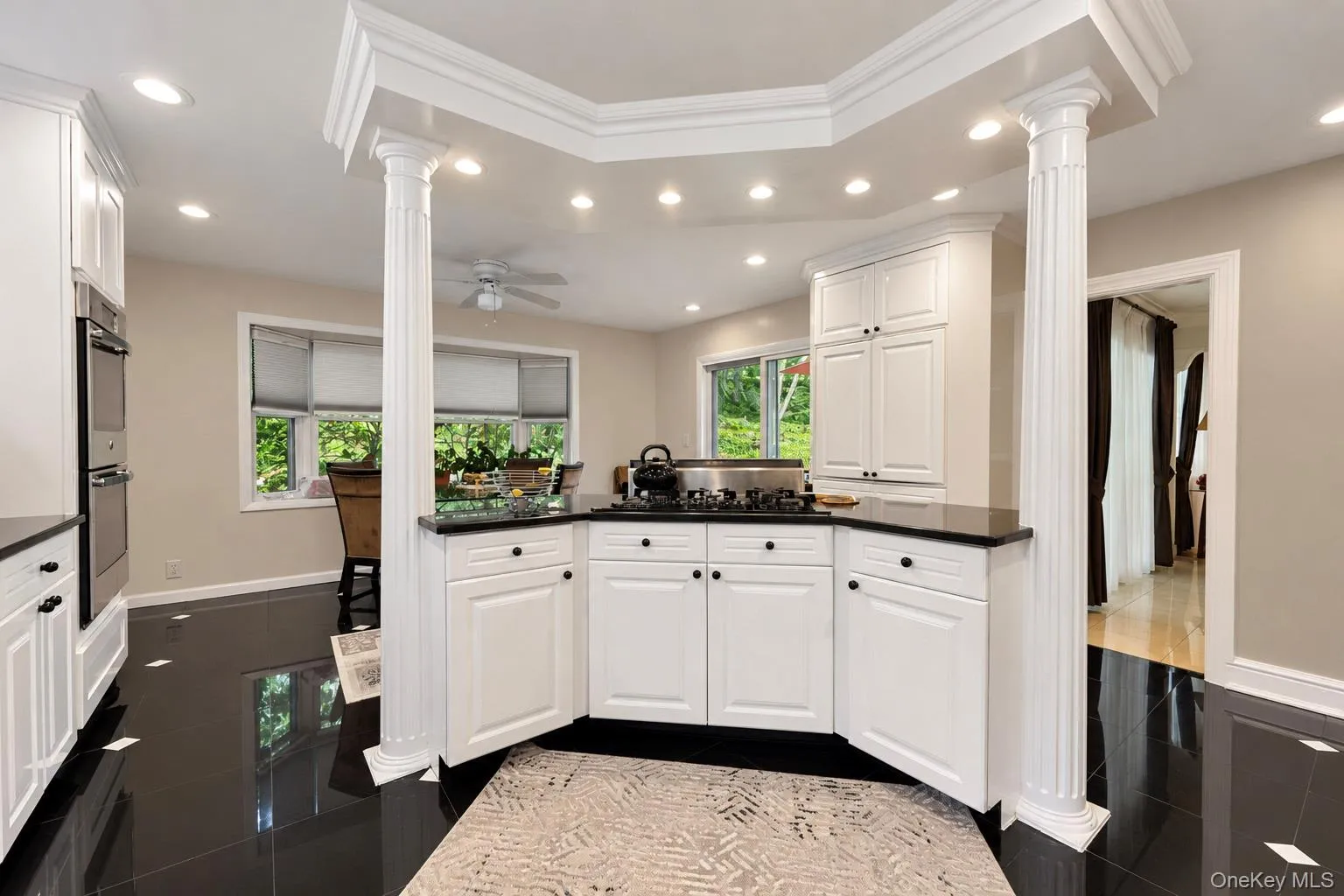 Kitchen featuring white shaker-style cabinetry, black stone countertops, integrated gas cooktop, recessed lighting, and decorative columns Kitchen featuring white shaker-style cabinetry, black stone countertops, integrated gas cooktop, recessed lighting, and decorative columns
