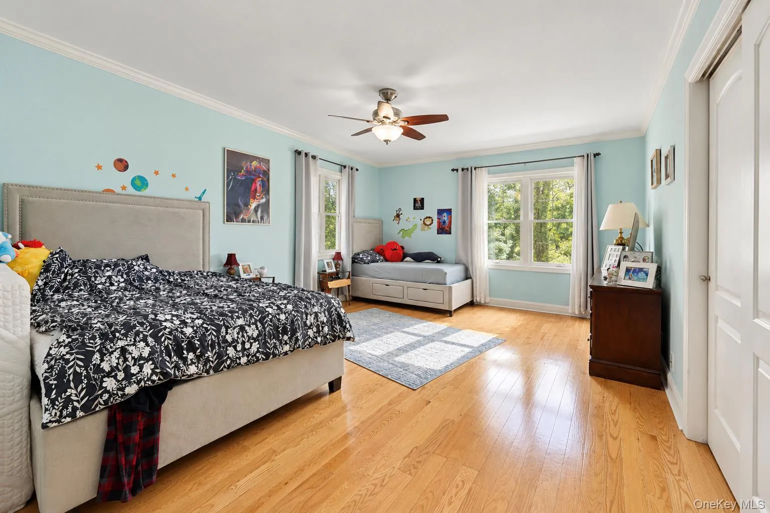 Spacious room featuring wood-finish flooring, crown molding, double-pane windows, and a central ceiling fan with integrated lighting Spacious room featuring wood-finish flooring, crown molding, double-pane windows, and a central ceiling fan with integrated lighting