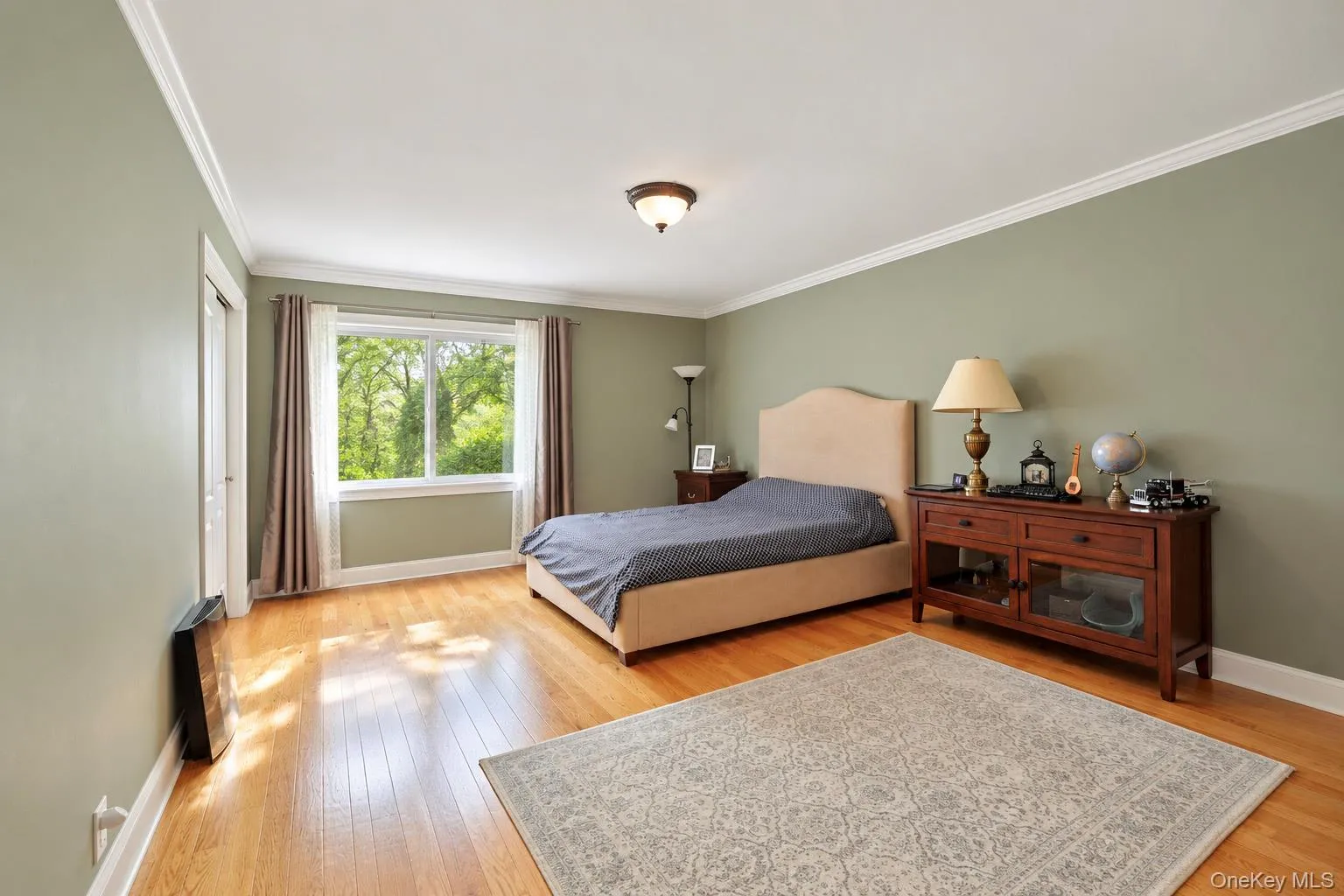 Spacious room featuring wood-finish flooring, crown molding, and a wide-pane window Spacious room featuring wood-finish flooring, crown molding, and a wide-pane window