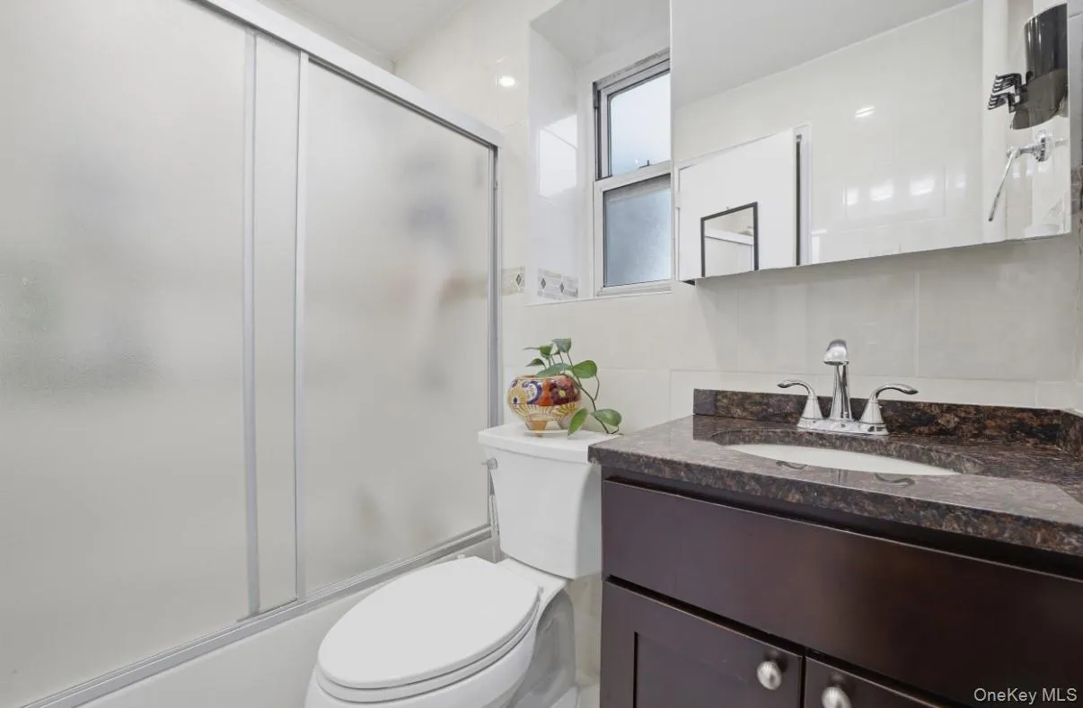 Bathroom featuring a dark wood-finish vanity with a stone countertop, an integrated oval sink, a wall-mounted mirrored medicine cabinet, and a walk-in shower with a frosted glass sliding door Bathroom featuring a dark wood-finish vanity with a stone countertop, an integrated oval sink, a wall-mounted mirrored medicine cabinet, and a walk-in shower with a frosted glass sliding door