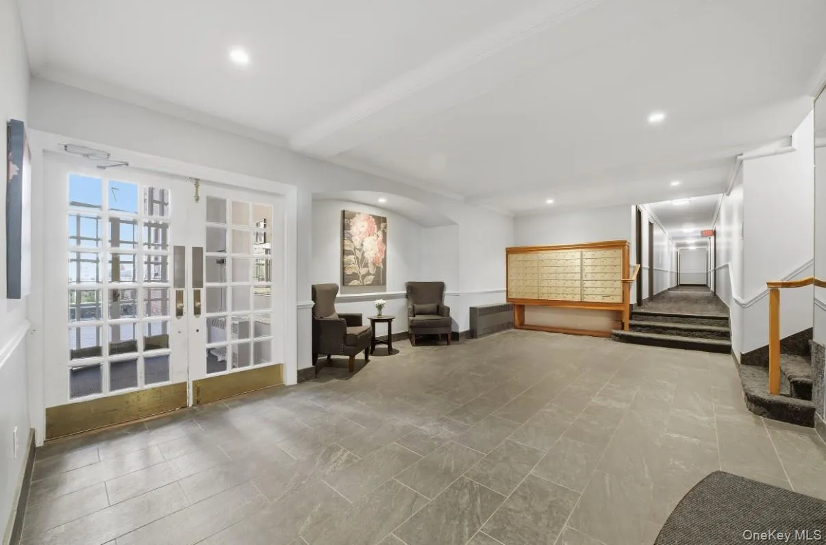 Building lobby featuring glass-paned double doors with brass kickplates, large-format tile flooring, recessed lighting, arched wall niche, and built-in mail collection center Building lobby featuring glass-paned double doors with brass kickplates, large-format tile flooring, recessed lighting, arched wall niche, and built-in mail collection center