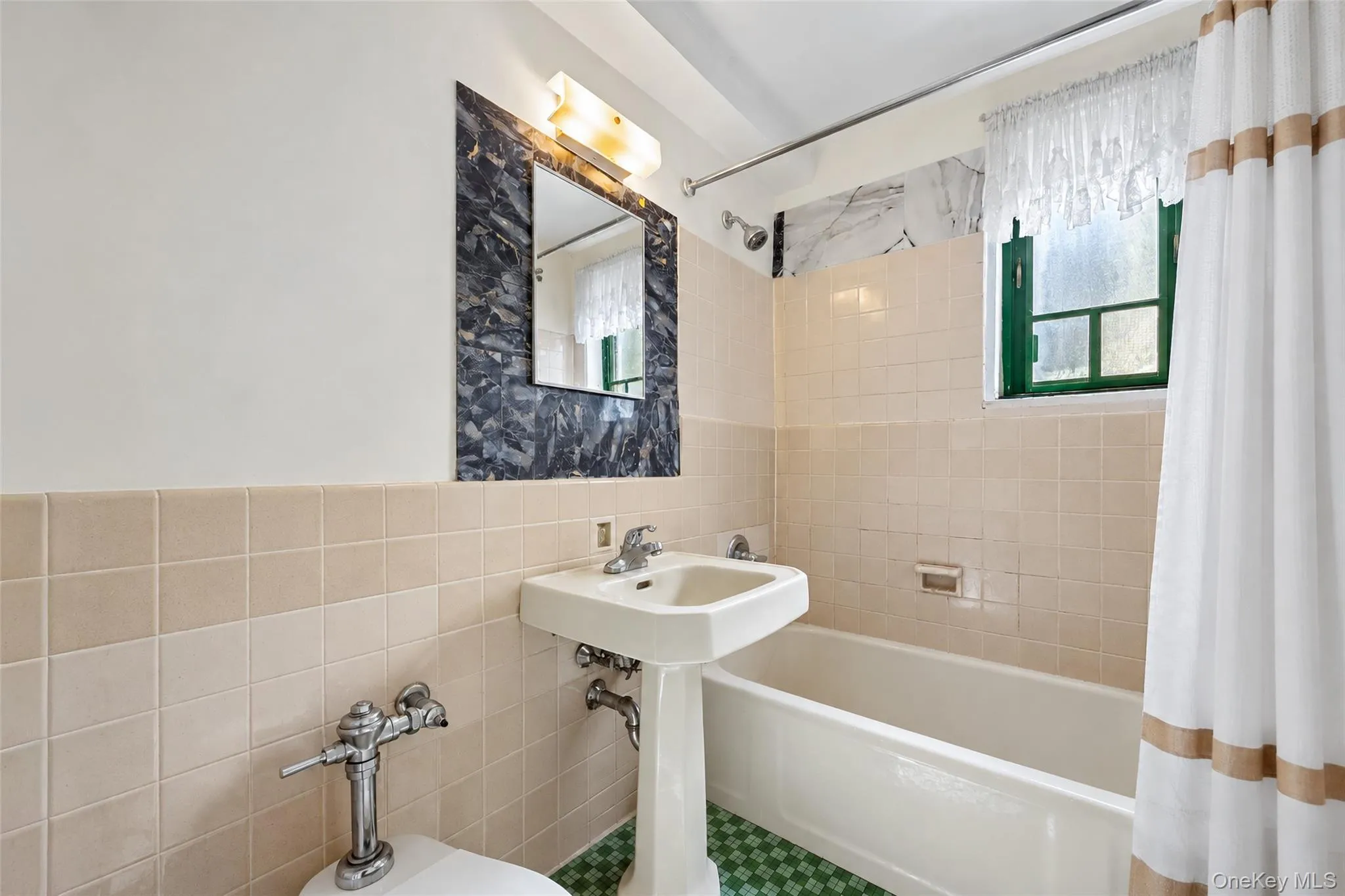 Bathroom featuring a white porcelain pedestal sink, tub with tiled surround, dark stone-finish accent wall, and wall-mounted lighting fixture Bathroom featuring a white porcelain pedestal sink, tub with tiled surround, dark stone-finish accent wall, and wall-mounted lighting fixture