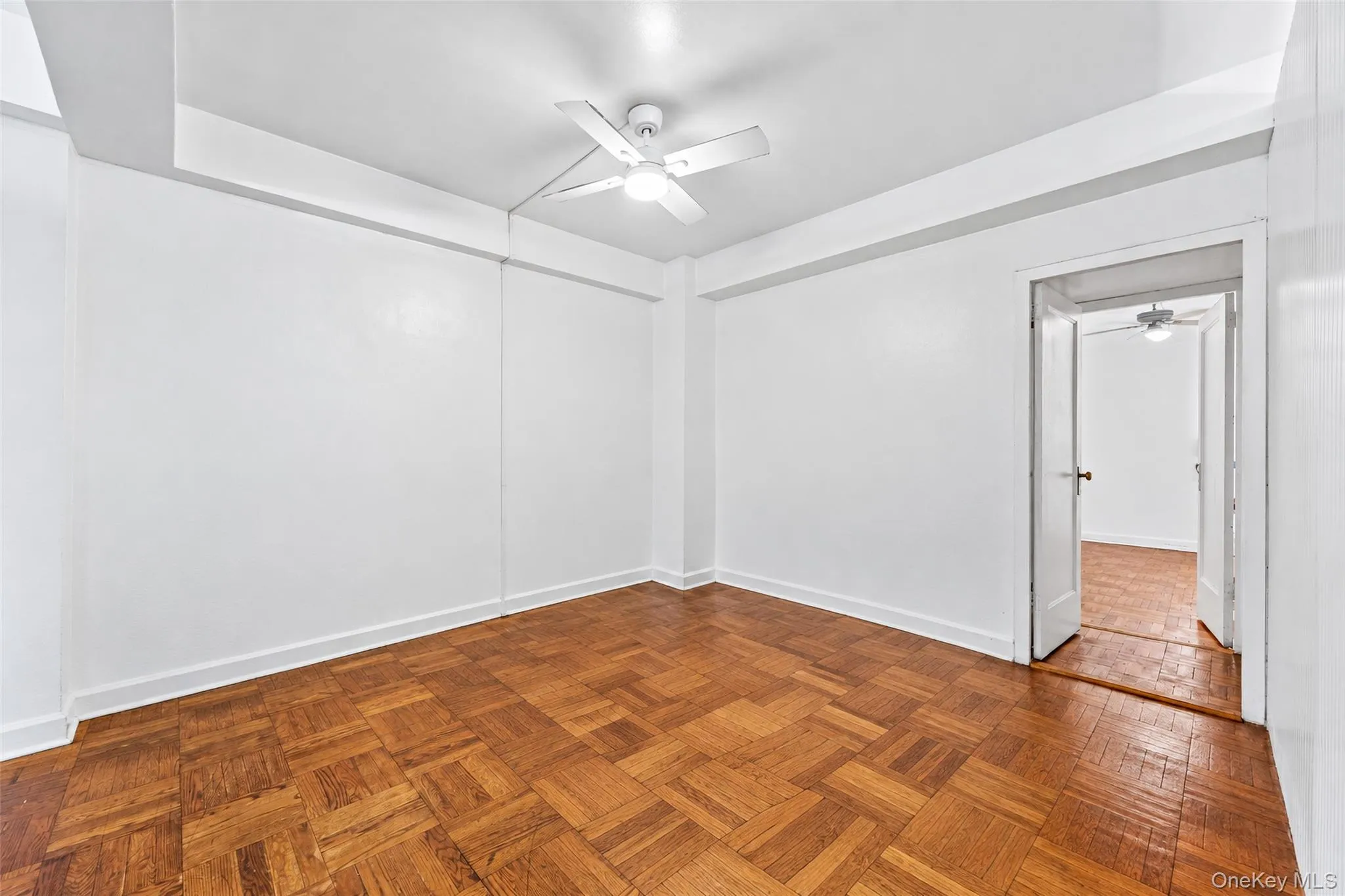 Interior room featuring parquet wood-finish flooring, high ceilings with crown molding, and an integrated ceiling fan with a light fixture Interior room featuring parquet wood-finish flooring, high ceilings with crown molding, and an integrated ceiling fan with a light fixture