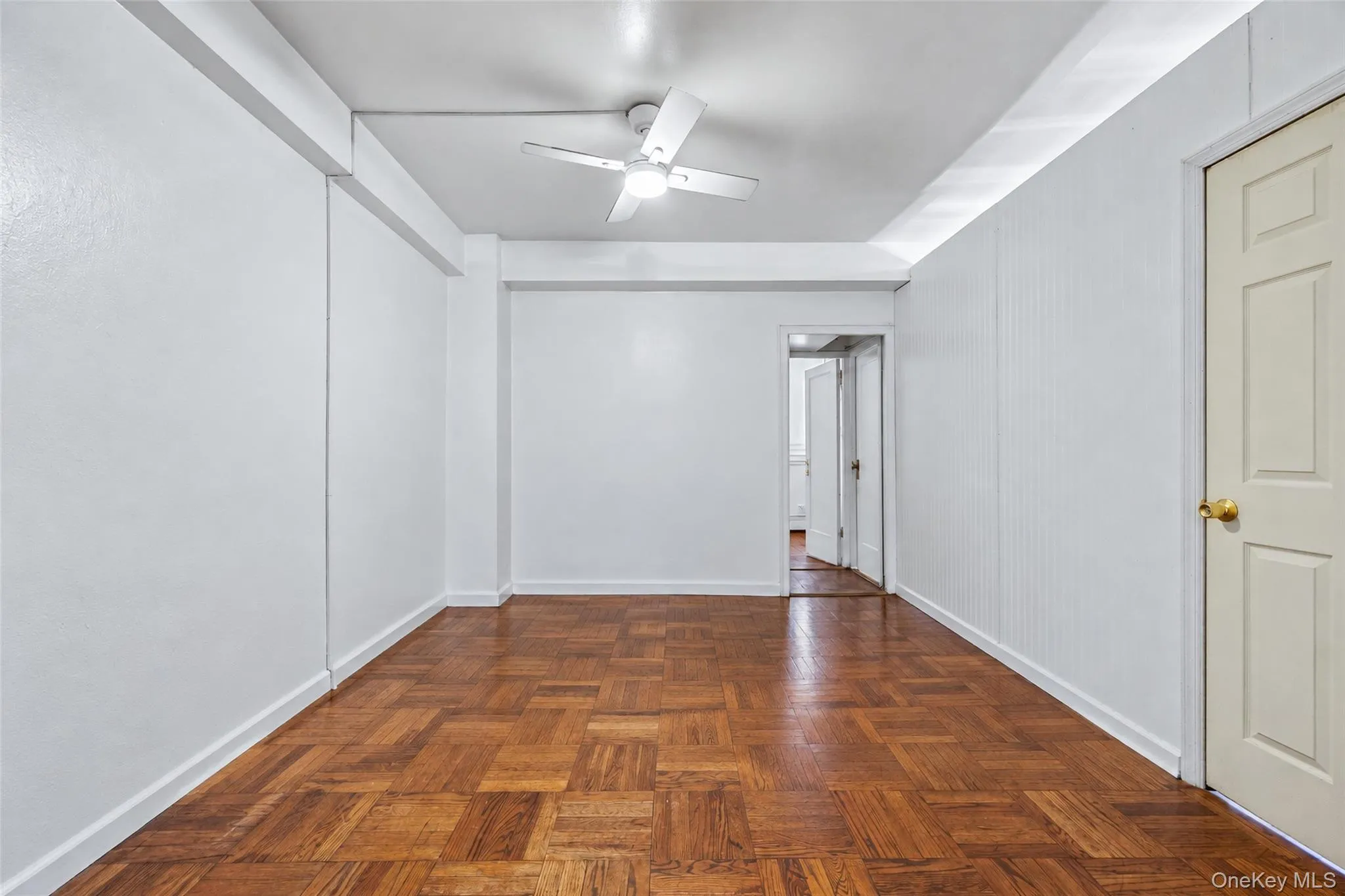 Parquet wood-finish flooring, white walls, and a ceiling-mounted light fixture with integrated fan blades Parquet wood-finish flooring, white walls, and a ceiling-mounted light fixture with integrated fan blades