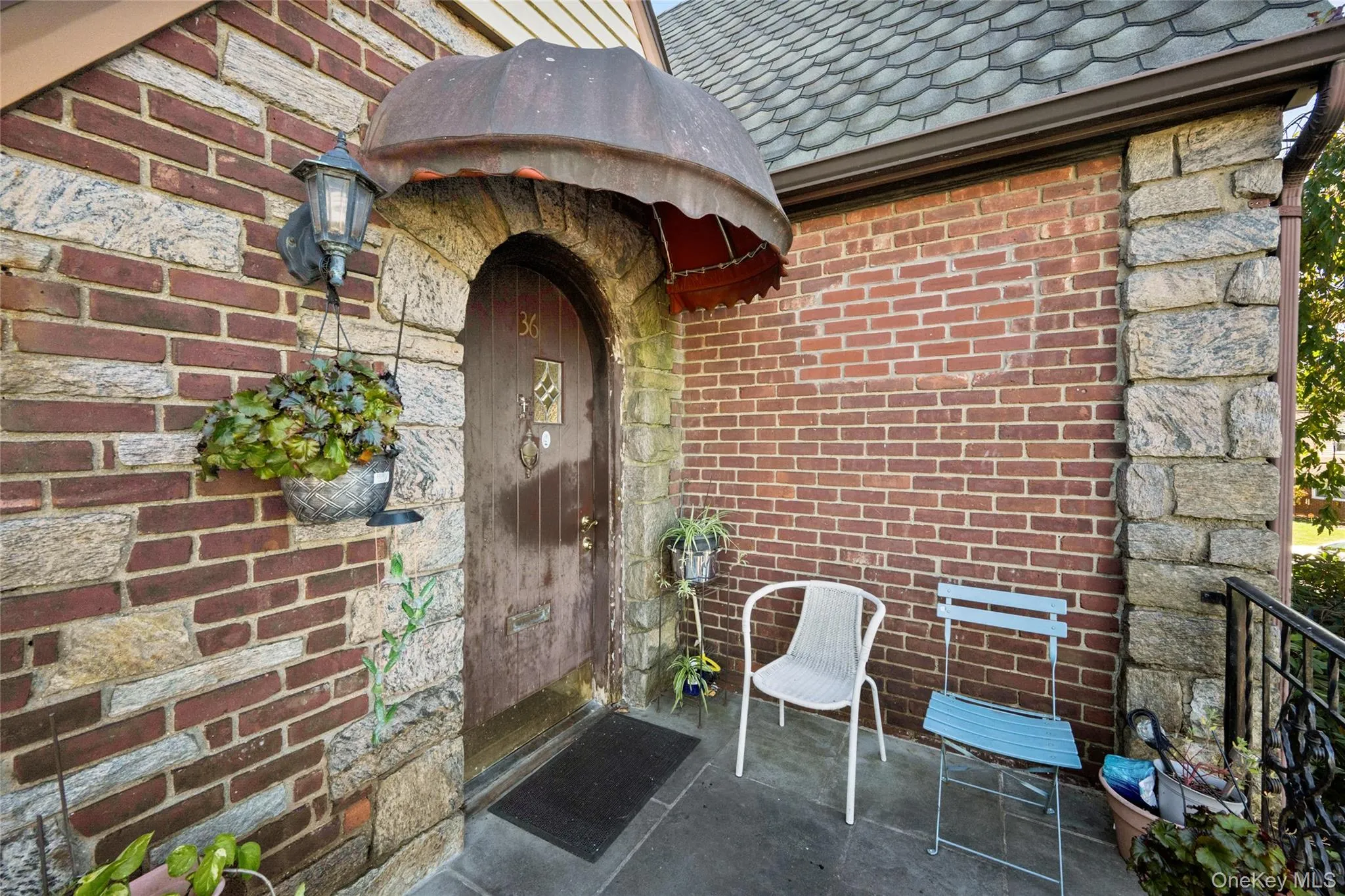 Exterior entryway featuring a brick and stone facade, arched stone doorway with a metal awning, and slate-finish flooring Exterior entryway featuring a brick and stone facade, arched stone doorway with a metal awning, and slate-finish flooring