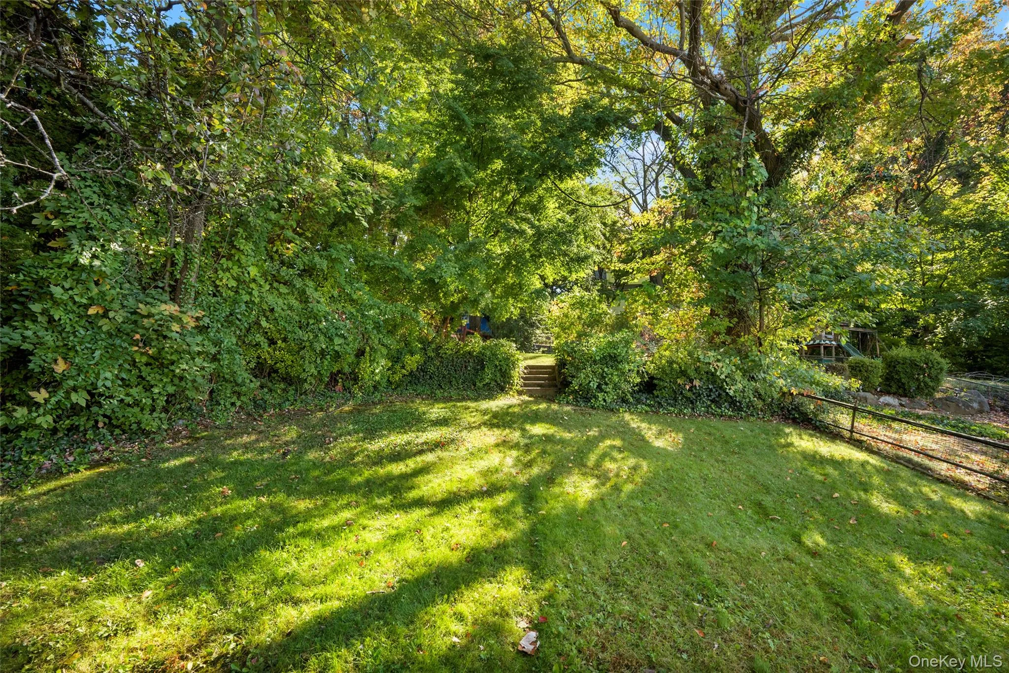 View from house looking toward the backyard featuring an expansive lawn, mature trees, tiered stone steps, and metal perimeter fencing View from house looking toward the backyard featuring an expansive lawn, mature trees, tiered stone steps, and metal perimeter fencing