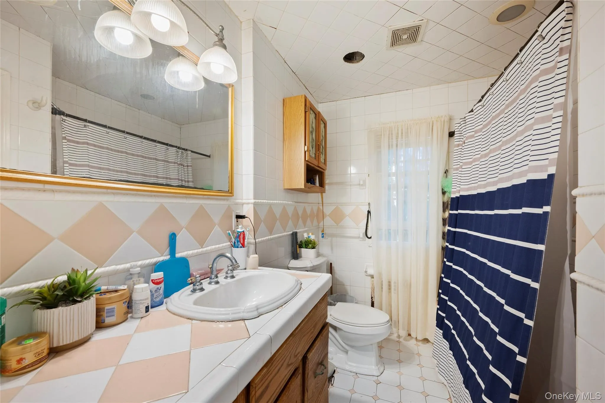 Bathroom featuring a vanity with an integrated basin, a wall-mounted medicine cabinet, a gold-toned mirror frame, and full-wall tile accents Bathroom featuring a vanity with an integrated basin, a wall-mounted medicine cabinet, a gold-toned mirror frame, and full-wall tile accents