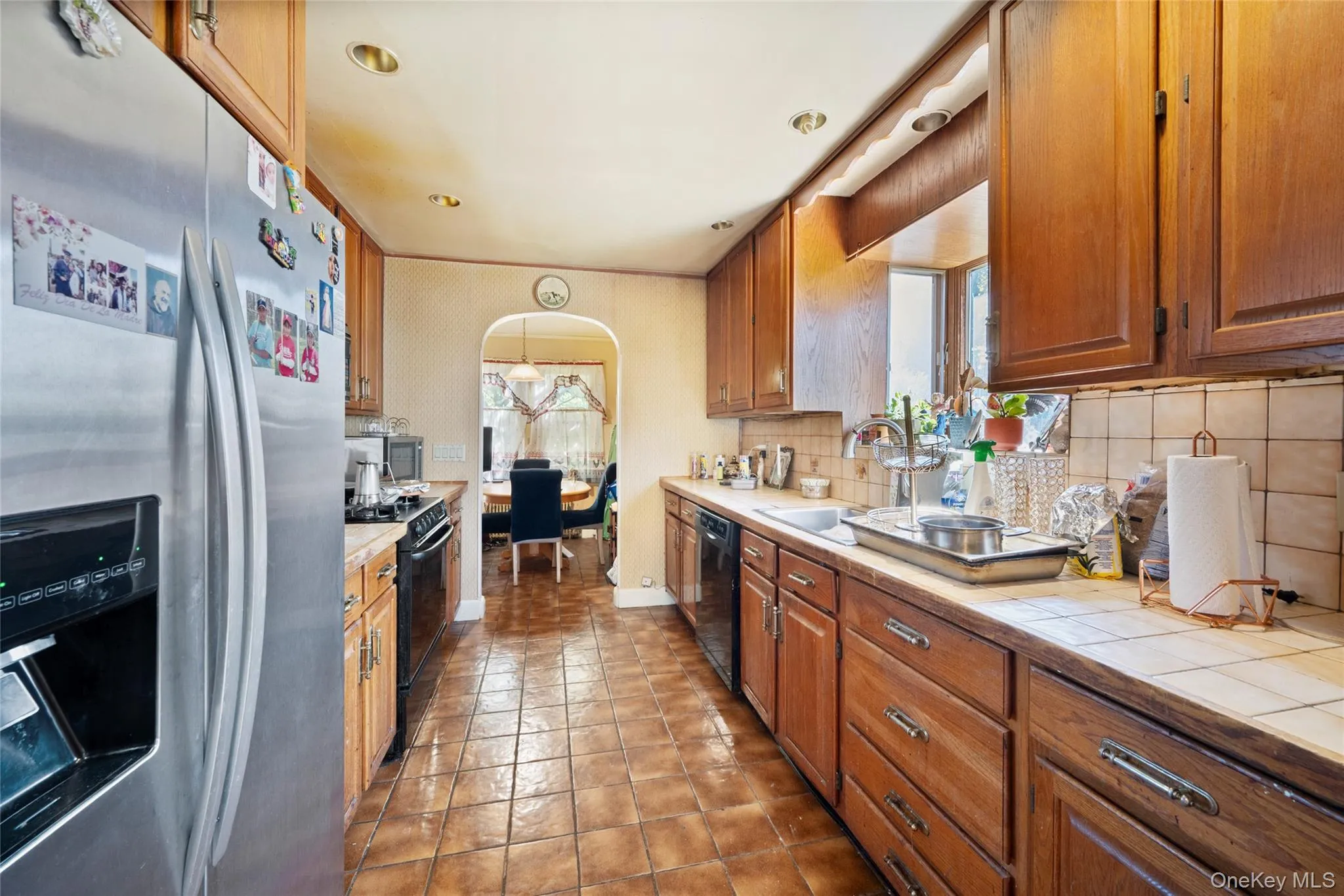 Kitchen featuring wood cabinetry, tile countertops, recessed lighting, tile flooring, and a stainless steel refrigerator Kitchen featuring wood cabinetry, tile countertops, recessed lighting, tile flooring, and a stainless steel refrigerator
