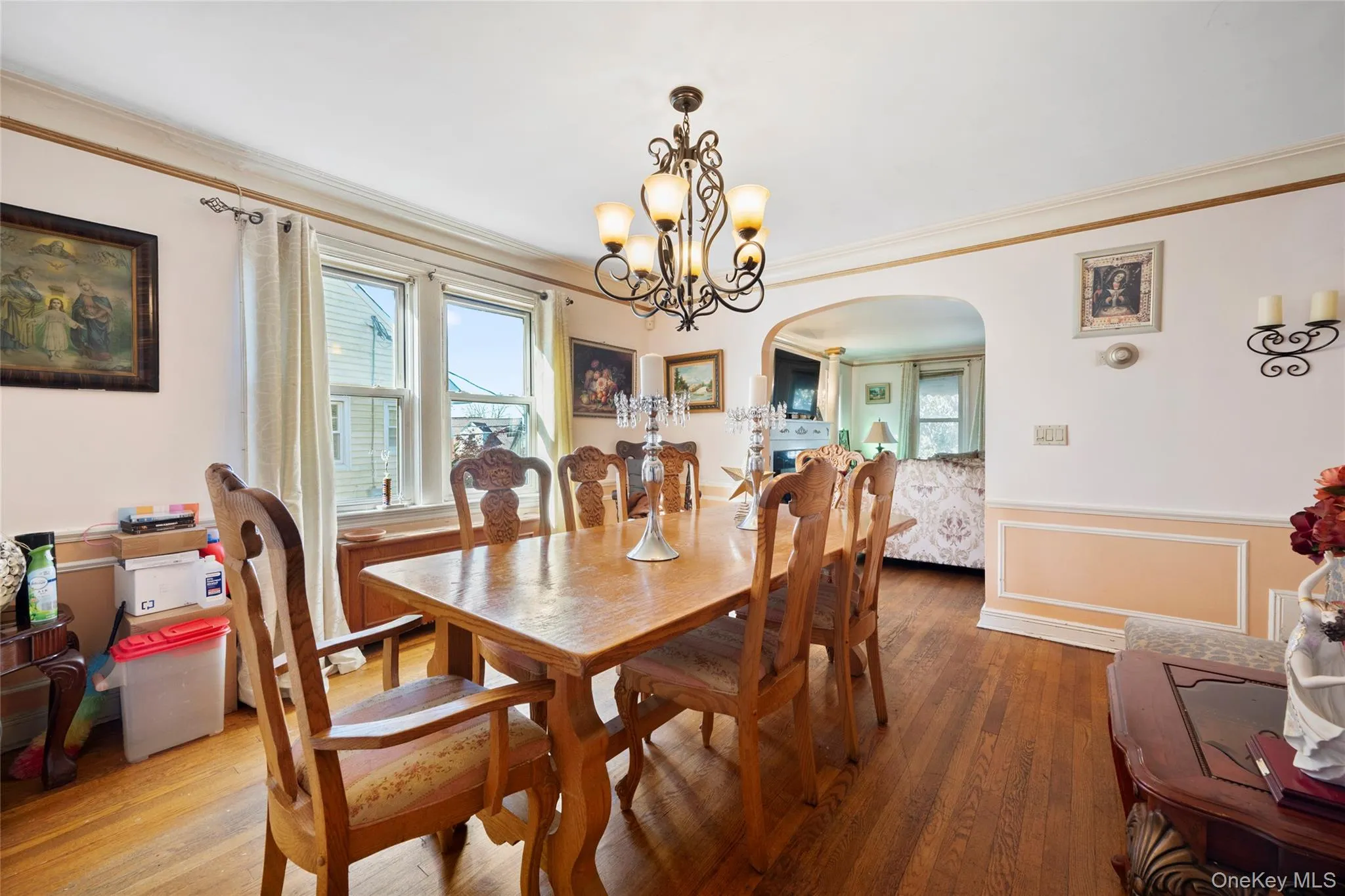 Dining area featuring wood-finish flooring, wainscoting, an arched doorway, and an ornate metal chandelier Dining area featuring wood-finish flooring, wainscoting, an arched doorway, and an ornate metal chandelier
